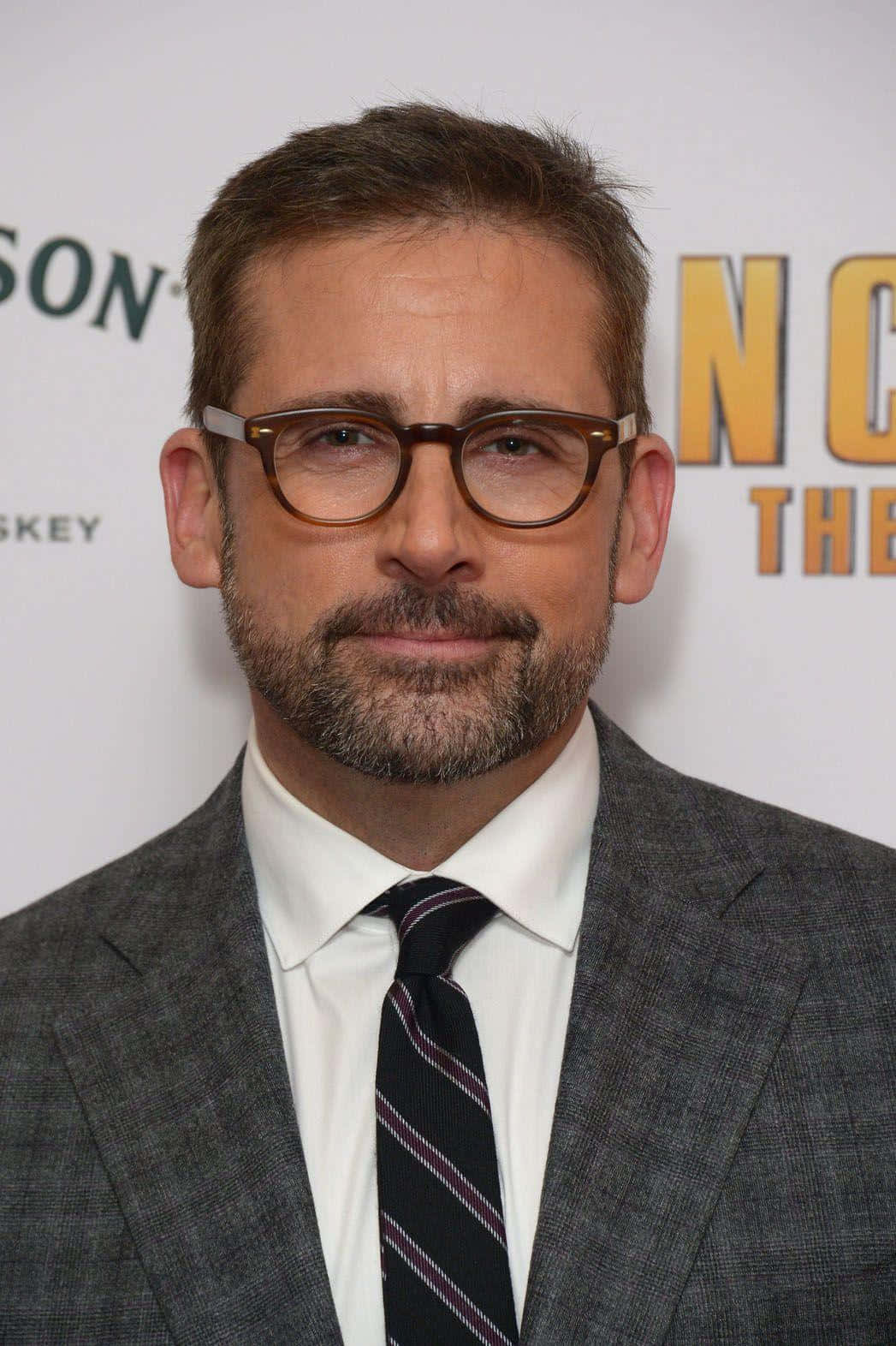 steve carell 桌布 壁紙 — 演員史提夫卡爾（Steve Carell）身穿俐落灰色西裝、戴眼鏡，在品牌背景的宣傳活動中。