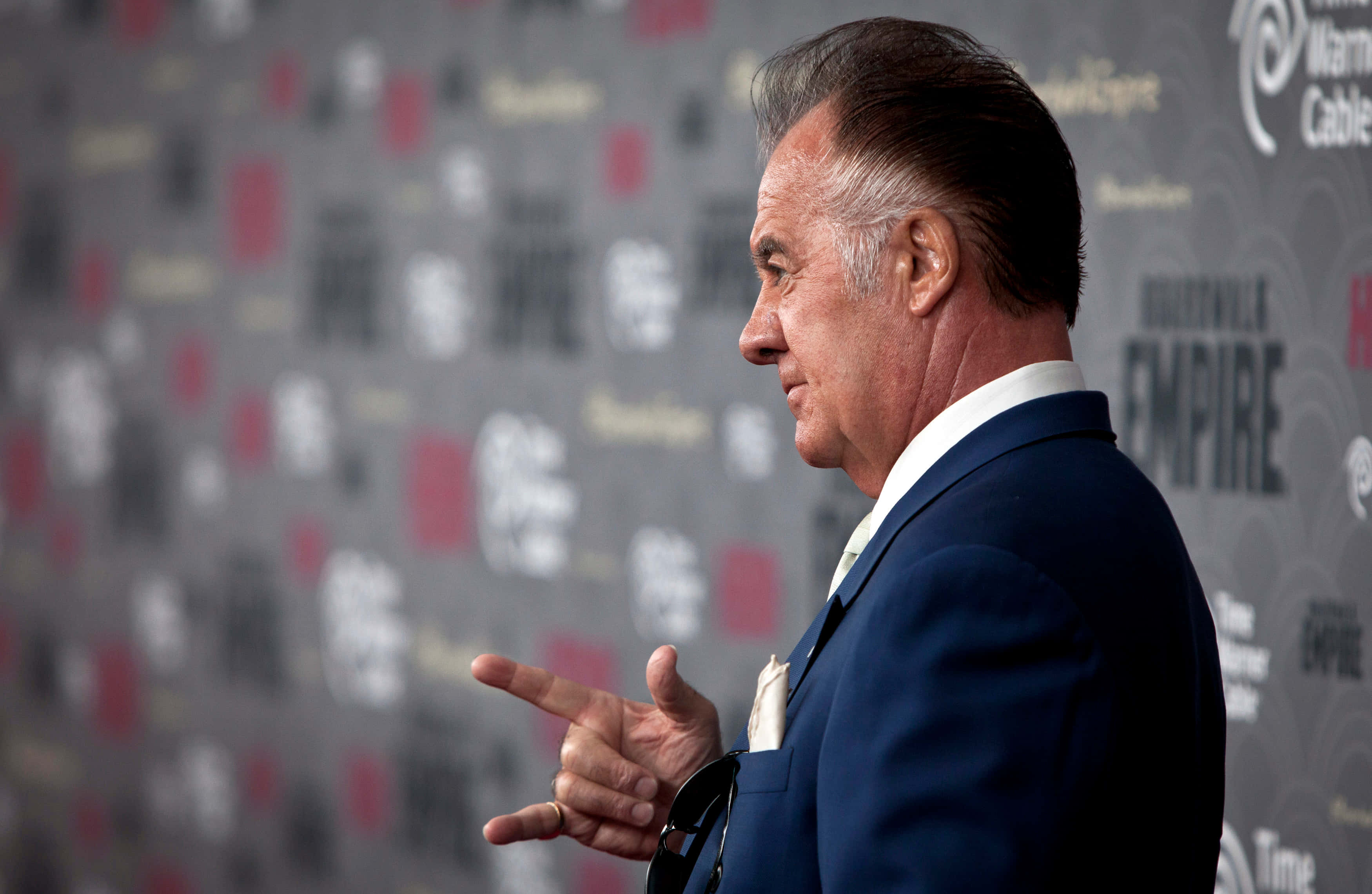 Tony Sirico 桌布 壁紙 — 演員喬·佩西身穿俐落藍色西裝，在模糊宣傳背景的紅地毯活動上自信地做手勢。