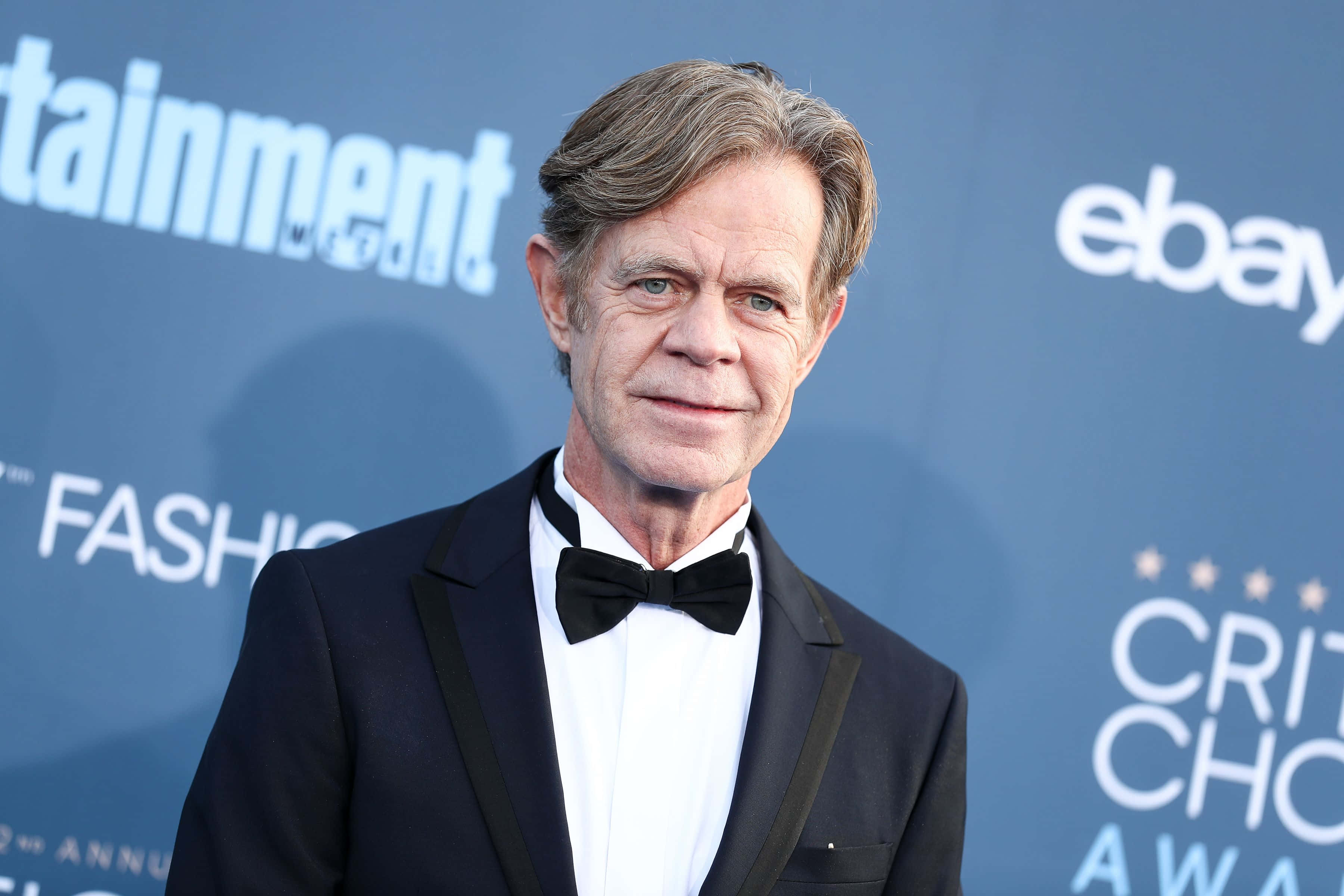 william h. macy 桌布 壁紙 — 演員威廉·H·梅西身穿黑色燕尾服配蝴蝶結，在帶有標誌的藍色活動背景前擺姿勢。