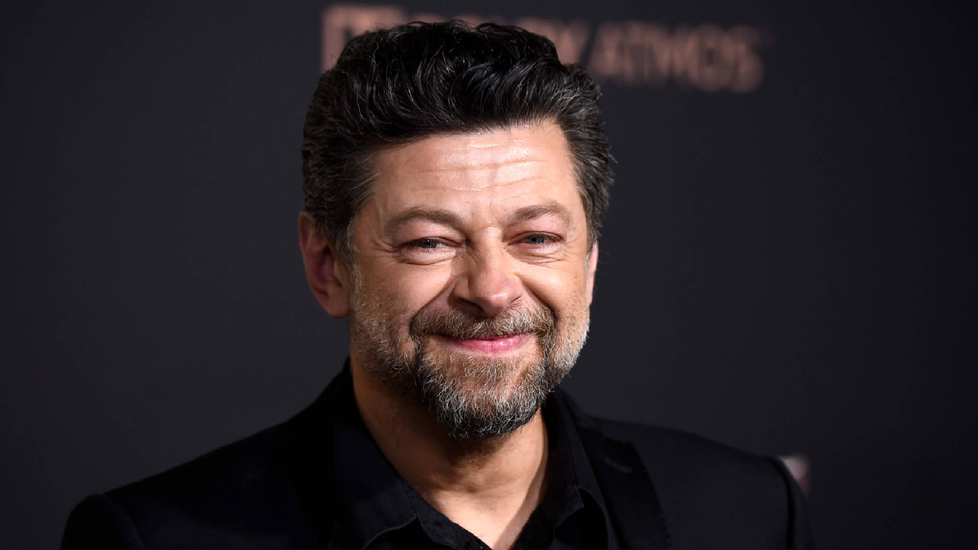 actor 桌布 壁紙 — 演員安迪·瑟克斯在黑暗背景及模糊文字前對著鏡頭溫暖微笑。