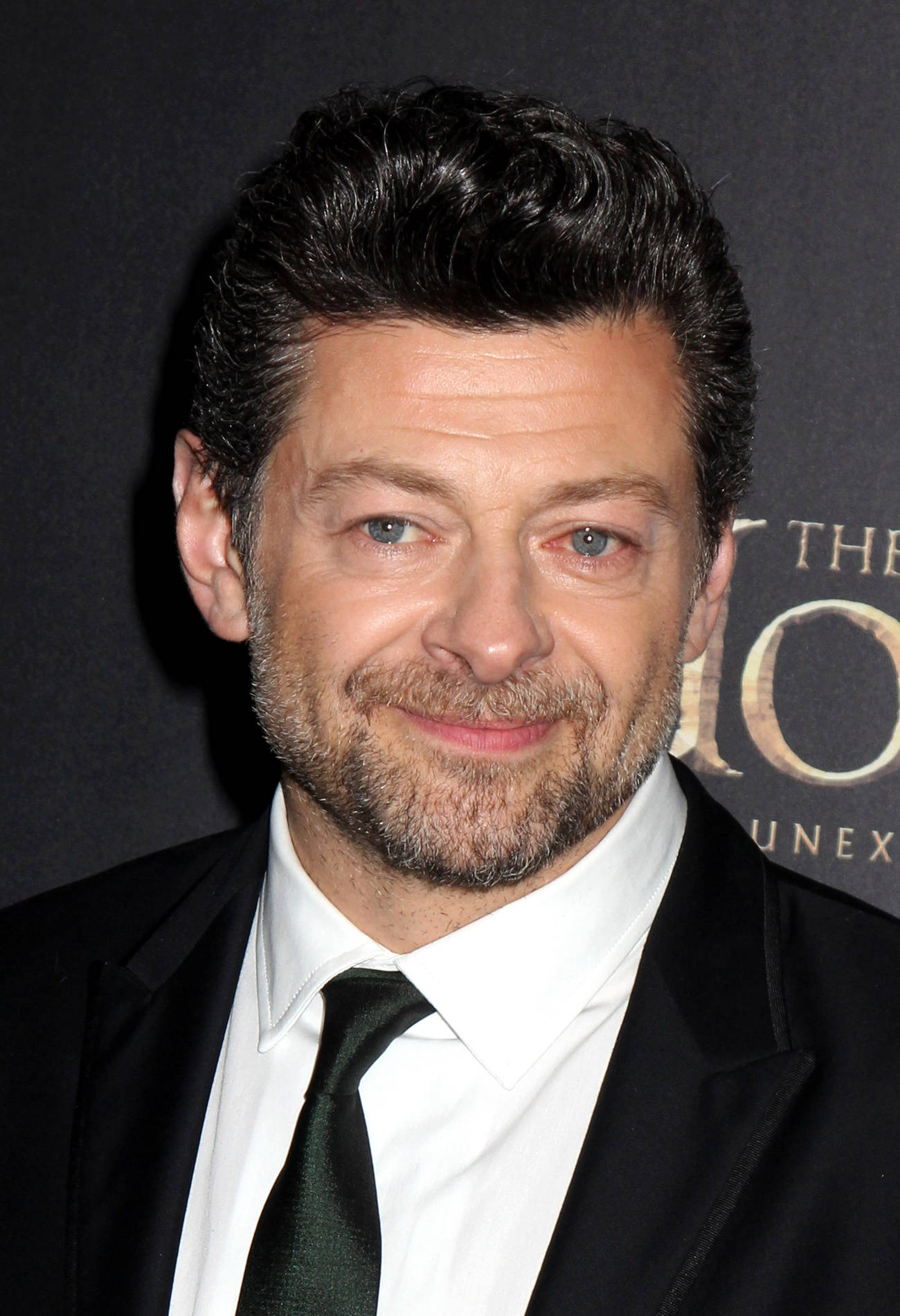 actor 桌布 壁紙 — 演員安迪·瑟克斯的近距離肖像，穿著黑色西裝和領帶，在深色背景下溫暖微笑。