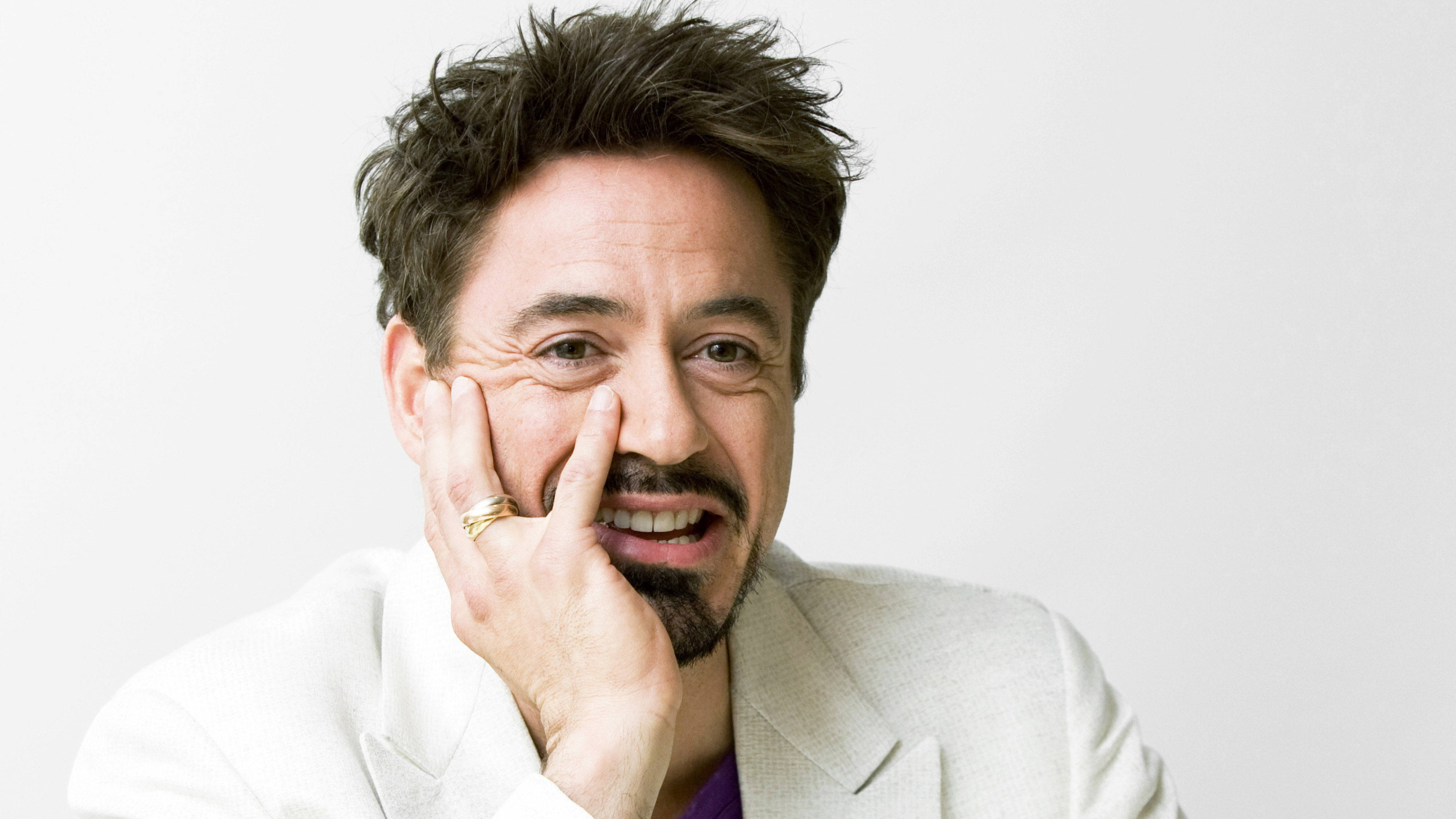 明星 桌布 壁紙 — 演員小勞勃·道尼（Robert Downey Jr.）在純白色背景上，將臉頰靠在手上，露出頑皮的笑容。