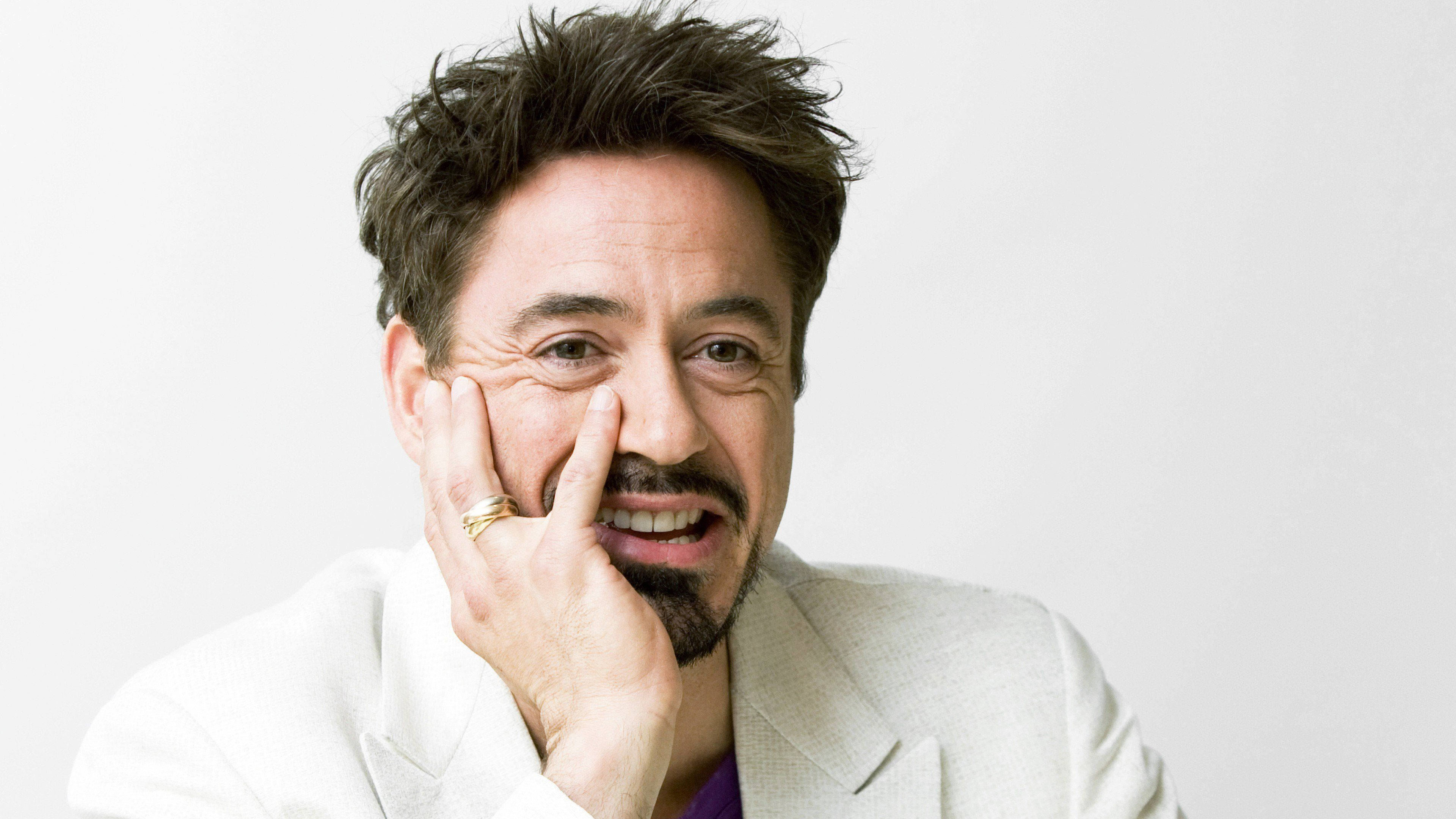 小勞勃·道尼 桌布 壁紙 — 演員小勞勃·道尼（Robert Downey Jr.）在純白色背景上，將臉頰靠在手上，露出頑皮的笑容。