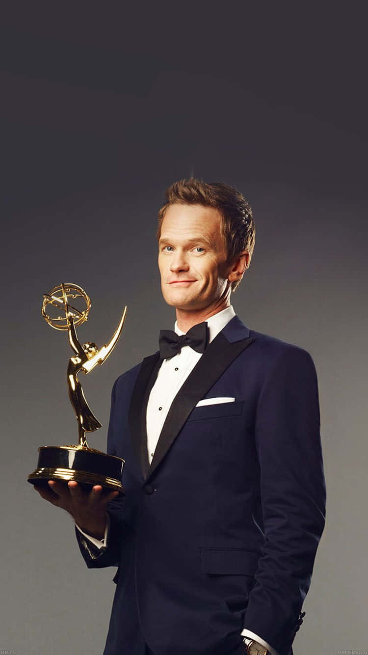 neil patrick harris 桌布 壁紙 — 演員尼爾·派屈克·哈里斯身穿海軍藍禮服，自信微笑地手持金色艾美獎，背景為深灰色攝影棚。