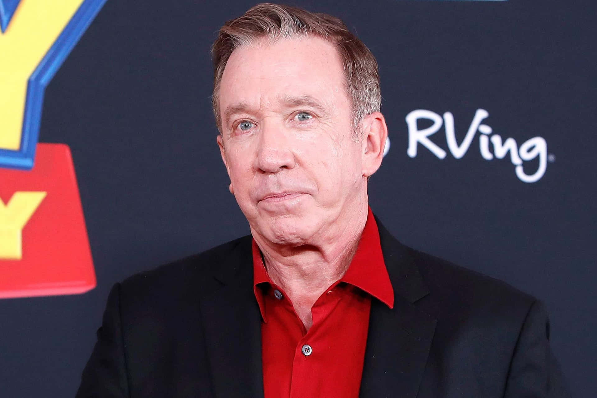 Tim Allen 桌布 壁紙 — 演員提姆·艾倫穿著黑色西裝和紅色襯衫，在深色背景前擺姿勢，帶有'RVing'標誌。