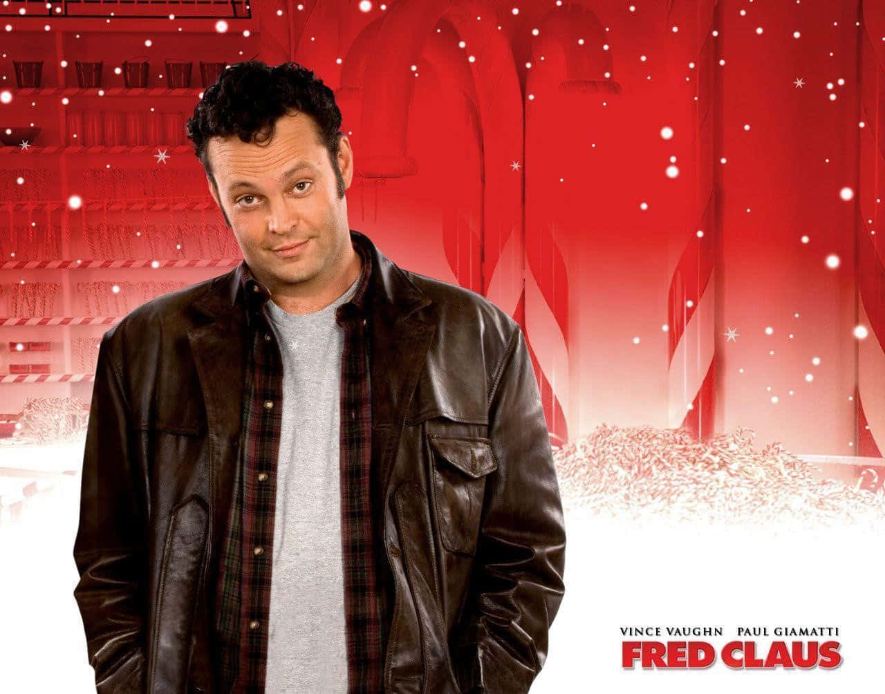 Vince Vaughn 桌布 壁紙 — 演員文斯·沃恩穿著皮夾克，在節日紅色糖果棒工廠背景下微笑，雪花飄落。