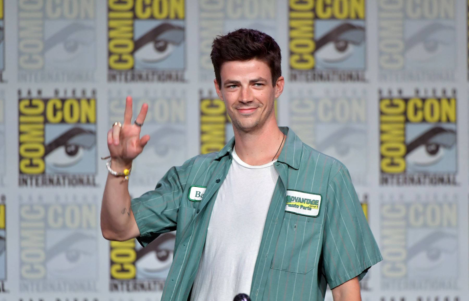 Grant Gustin 桌布 壁紙 — 演員格蘭特·古斯汀在Comic-Con微笑揮手，身穿綠色鈕扣襯衫，佩戴「Barry」名牌。
