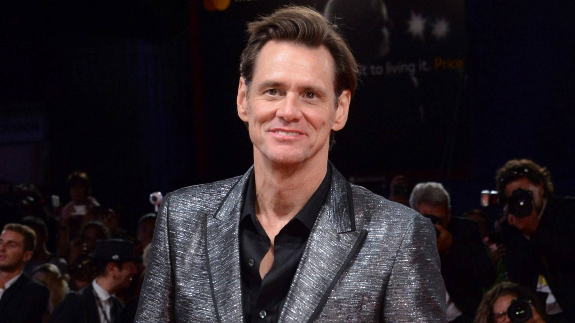 Jim Carrey 桌布 壁紙 — 演員比爾·普曼在明亮燈光下，於擁擠的活動中穿著閃亮的銀色西裝外套，自信地微笑。