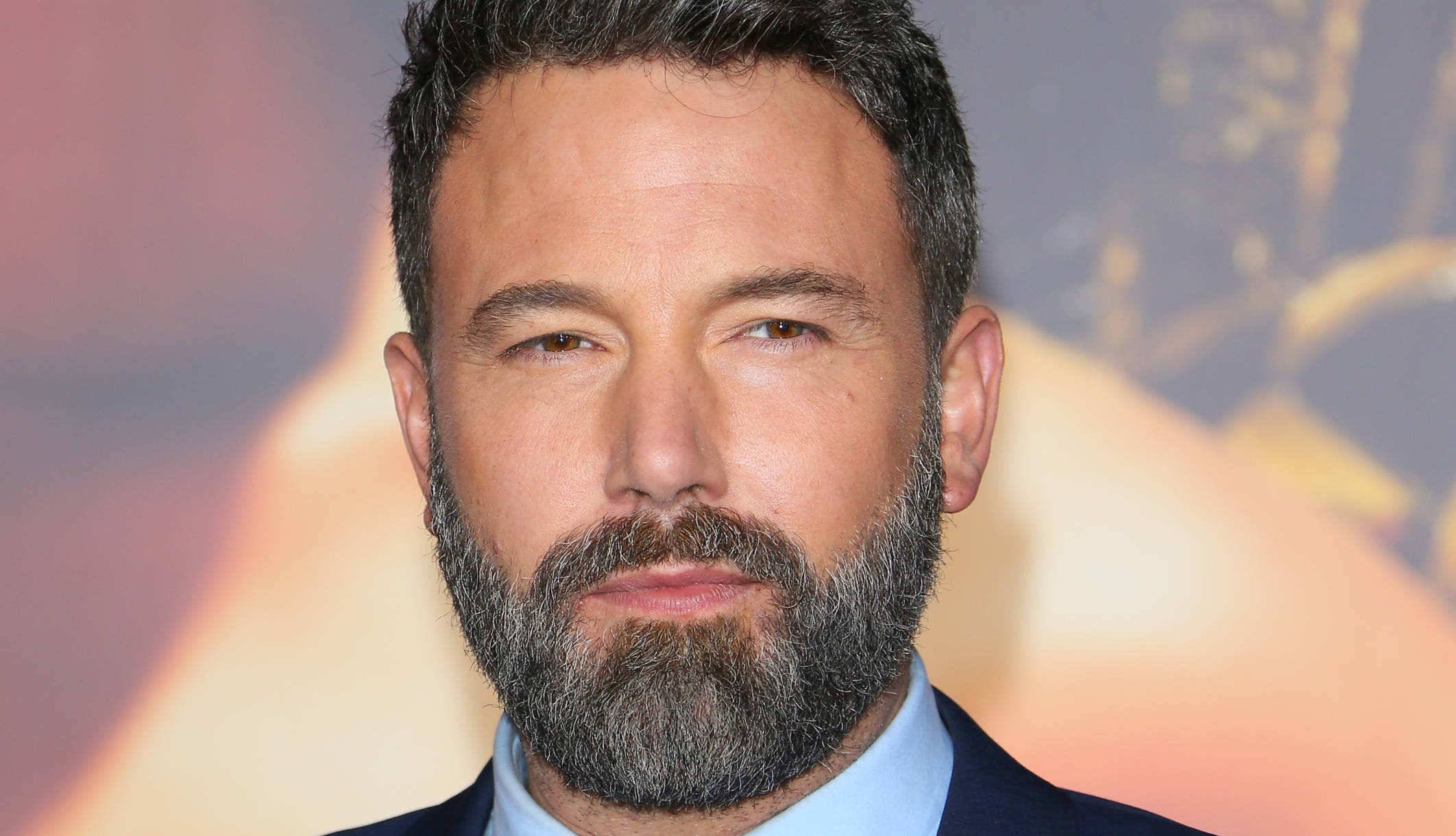 Ben Affleck 桌布 壁紙 — 演員班·艾佛列克的特寫肖像，留著灰白鬍鬚，穿著西裝，背景溫暖模糊。