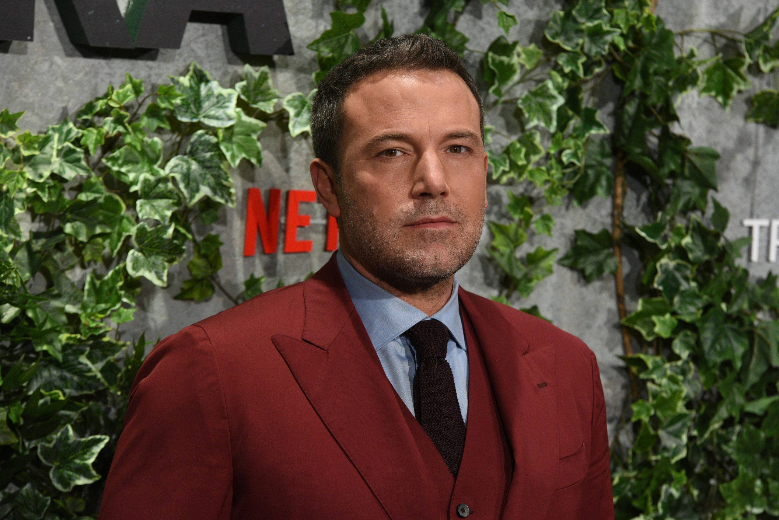 Ben Affleck 桌布 壁紙 — 演員班·艾佛列克身穿鮮紅色西裝，站在綠色常春藤牆前，牆上有紅色Netflix標誌。