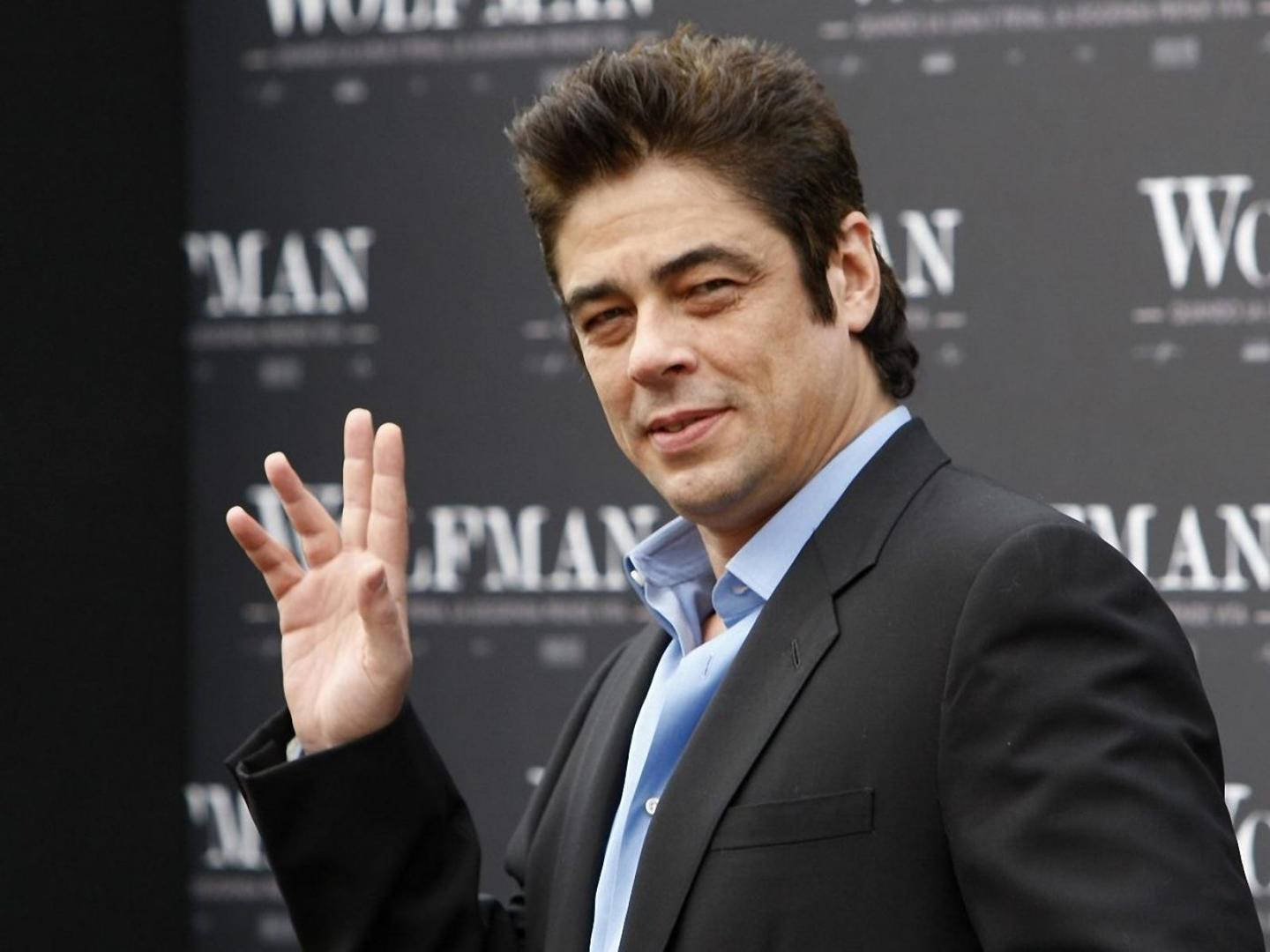 Celebrity 桌布 壁紙 — 演員班尼西奧·狄·托羅穿著黑色西裝和淺藍色襯衫，在《狼人》電影背景前向鏡頭揮手。