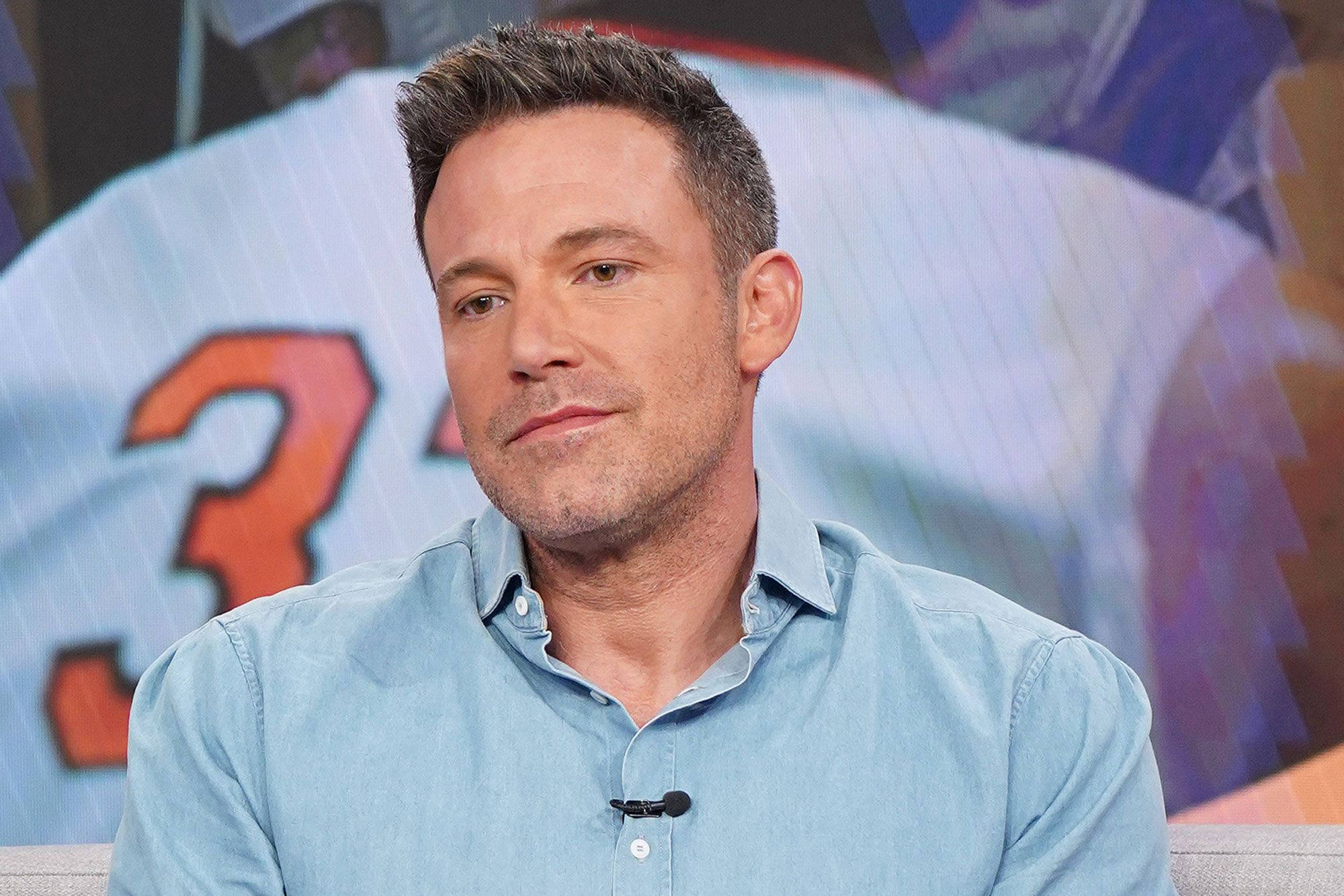 Ben Affleck 桌布 壁紙 — 演員班艾佛列克身穿淺藍色襯衫，坐在模糊的運動球衣背景前，球衣上有數字三。