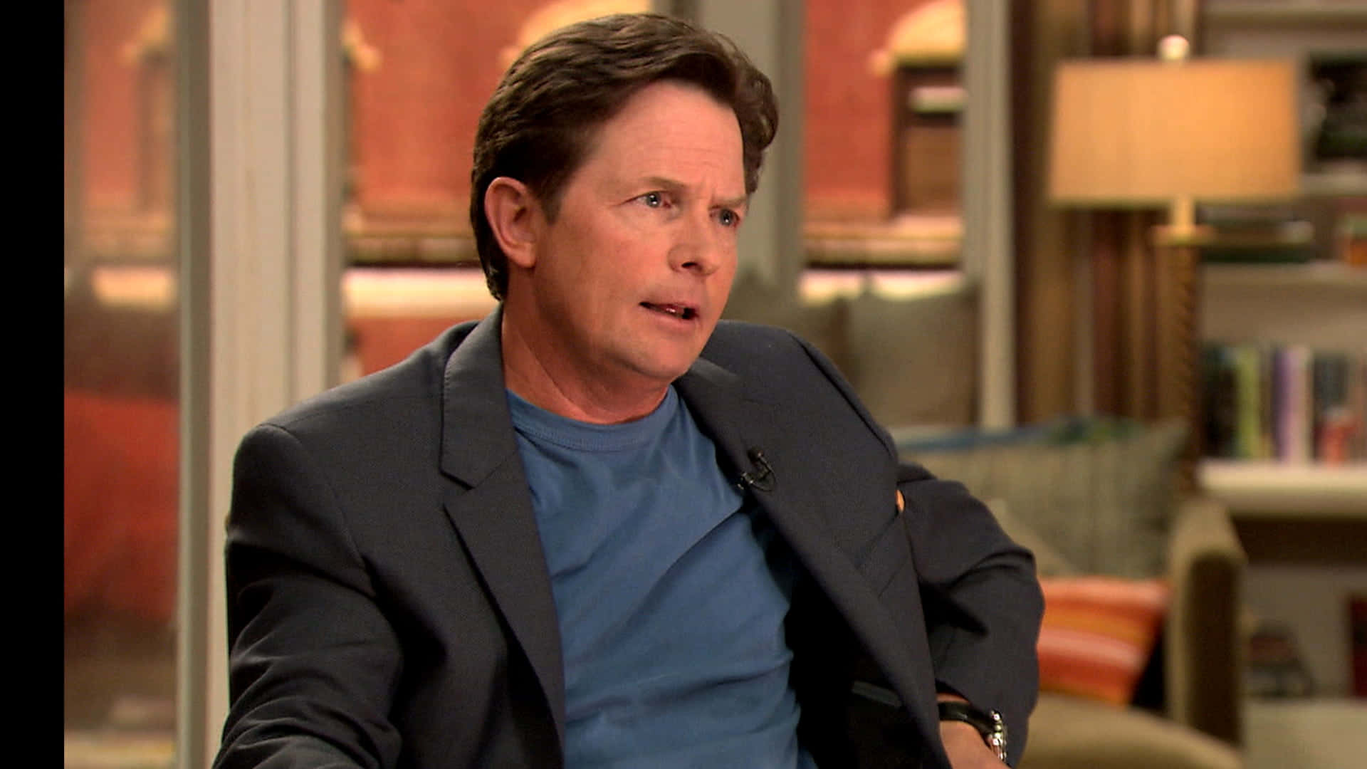 michael j fox 桌布 壁紙 — 演員米高·J·福克斯在訪問期間坐在舒適的錄影室椅子上，身穿藍色T恤和深色西裝外套。