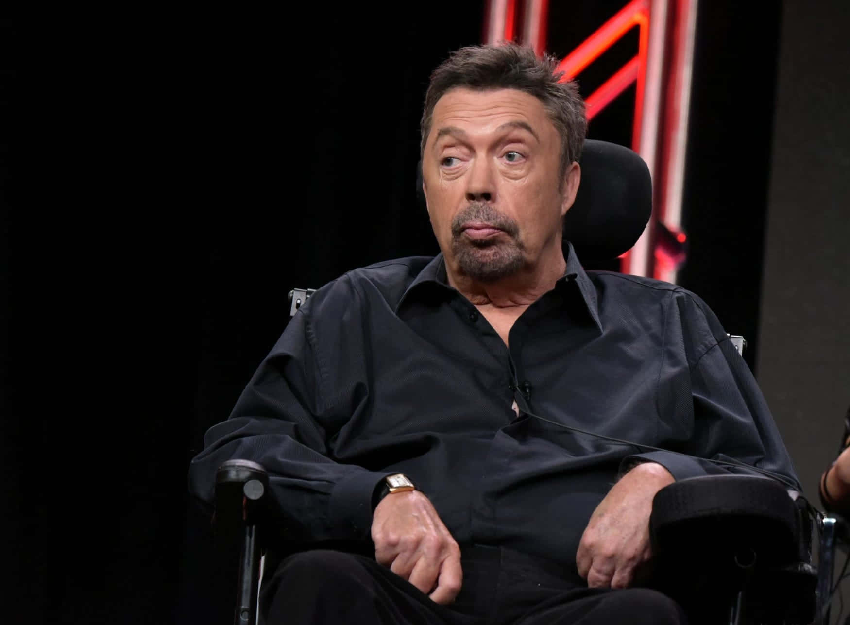 Tim Curry 桌布 壁紙 — 演員蓋瑞·歐德曼坐在黑色椅子上，背景昏暗，身後有紅色霓虹燈光。