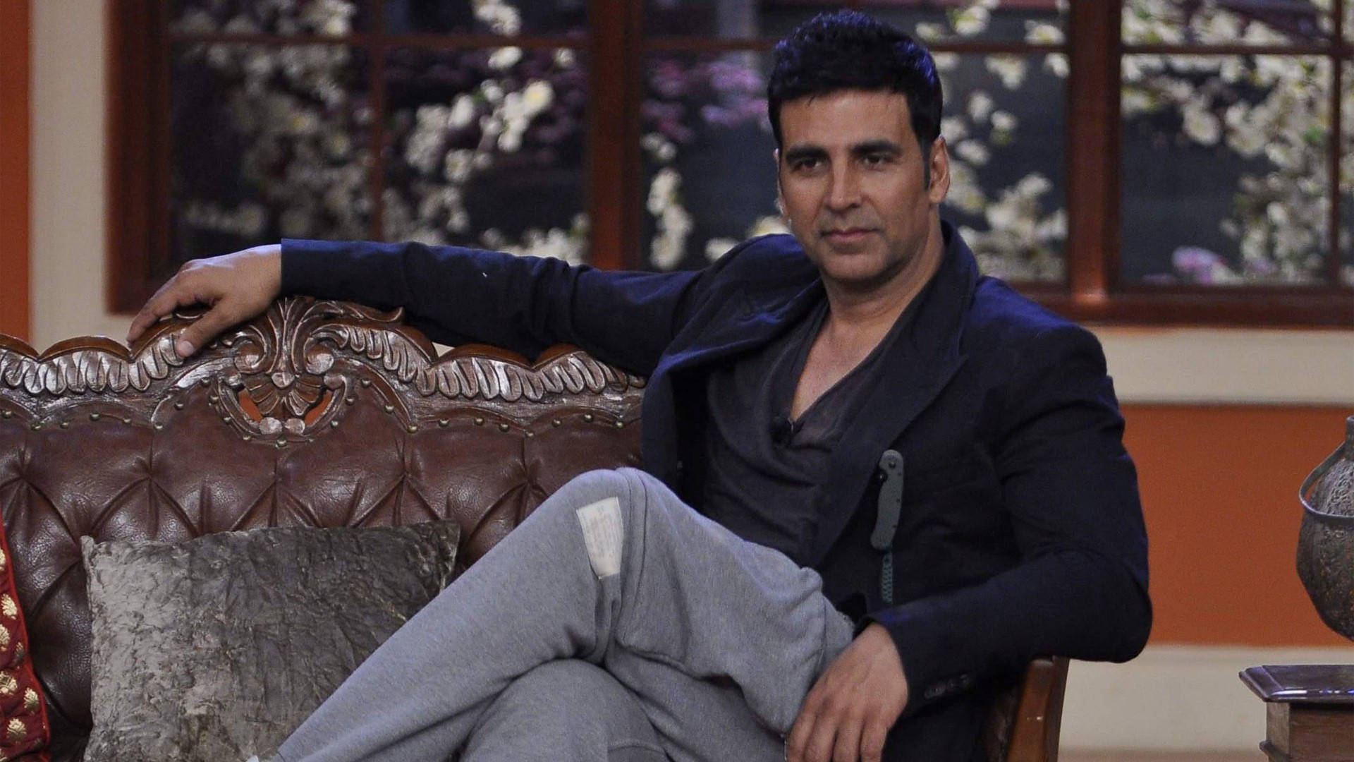 Akshay Kumar 桌布 壁紙 — 演員阿克謝·庫馬爾隨意地靠在一張華麗的棕色皮沙發上，背景是花卉窗戶。