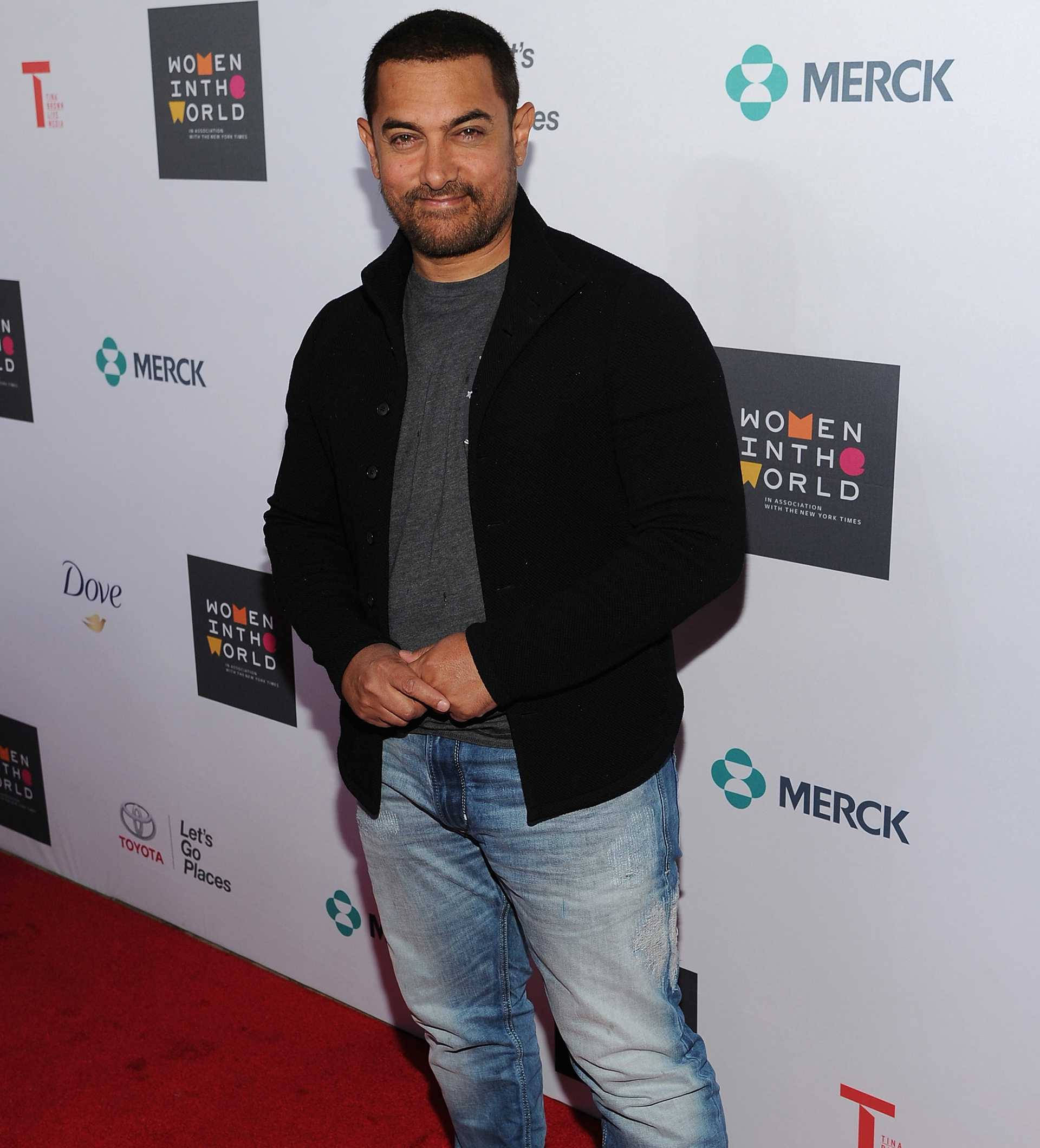 Aamir Khan 桌布 壁紙 — 演員阿米爾·汗在Women in the World活動的紅地毯上自信微笑，背景帶有品牌標誌。