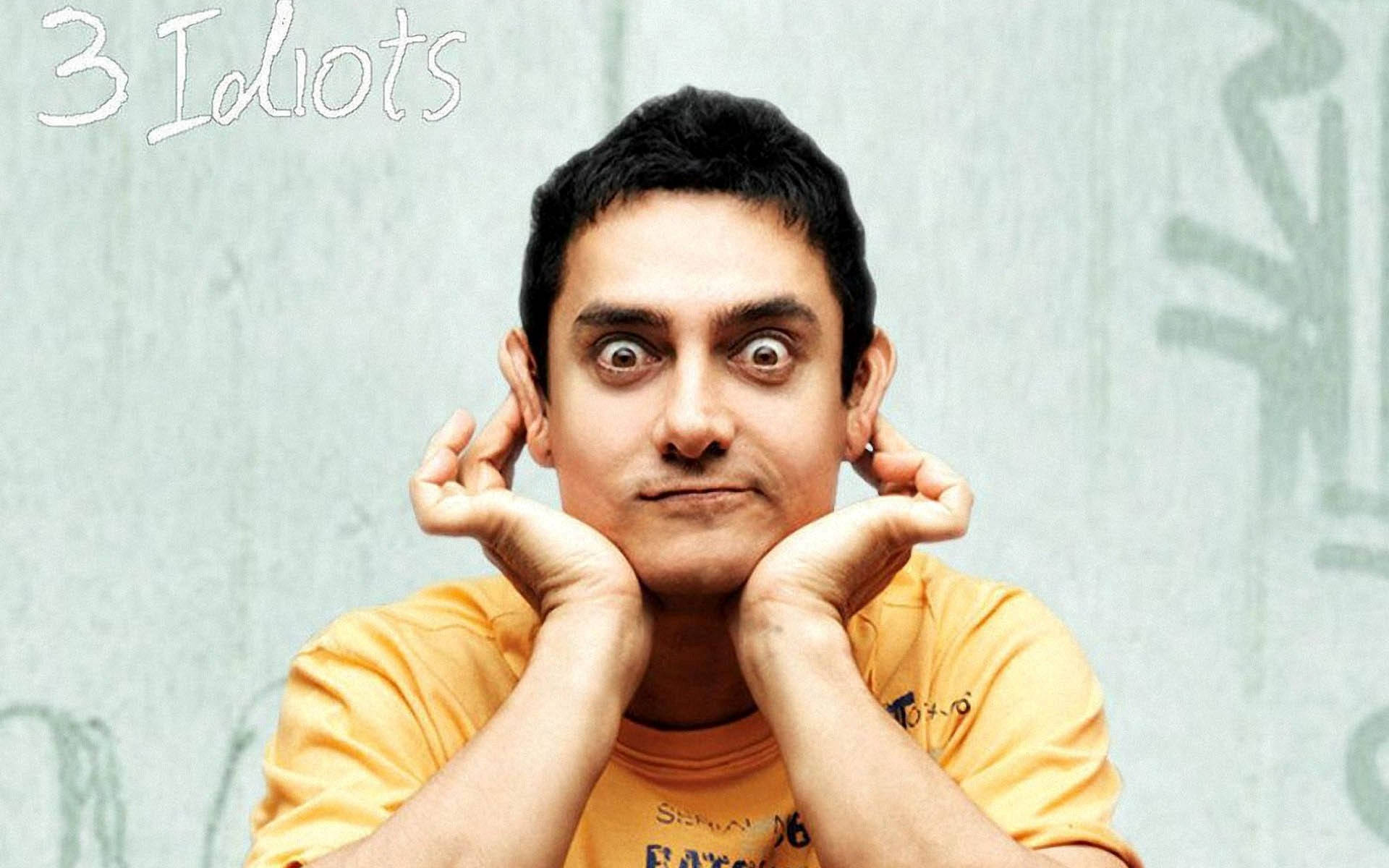 Aamir Khan 桌布 壁紙 — 演員阿米爾·汗身穿黃色T恤，雙手捧著臉頰，對著塗鴉牆做出驚訝的表情。