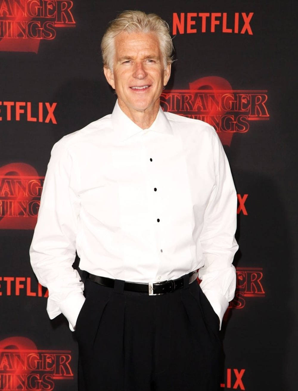 Netflix 桌布 壁紙 — 演員馬修·莫迪恩在Netflix《怪奇物語》活動中穿著白襯衫和黑褲自信微笑。