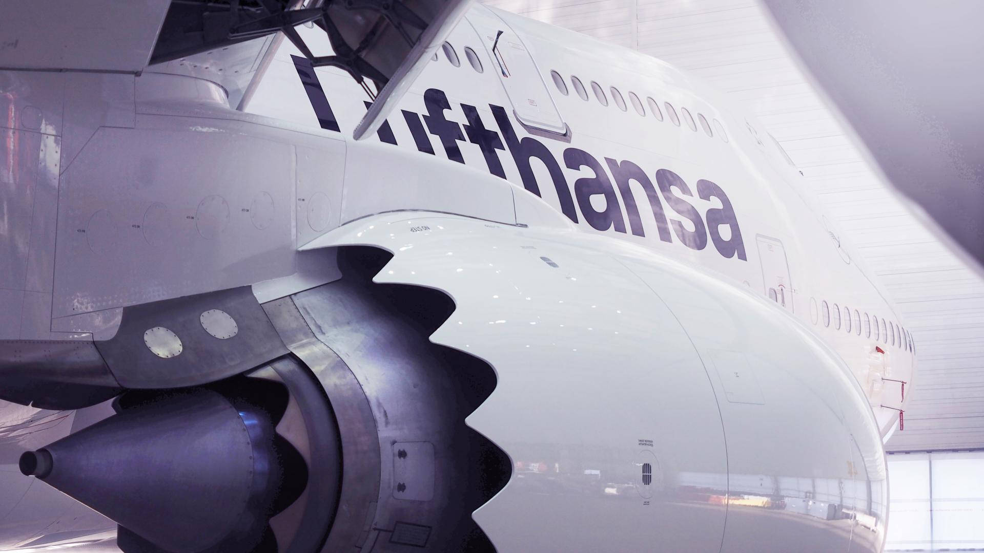 飛機 桌布 壁紙 — 漢莎航空飛機引擎和機身在明亮機庫內的特寫，帶有反光表面。