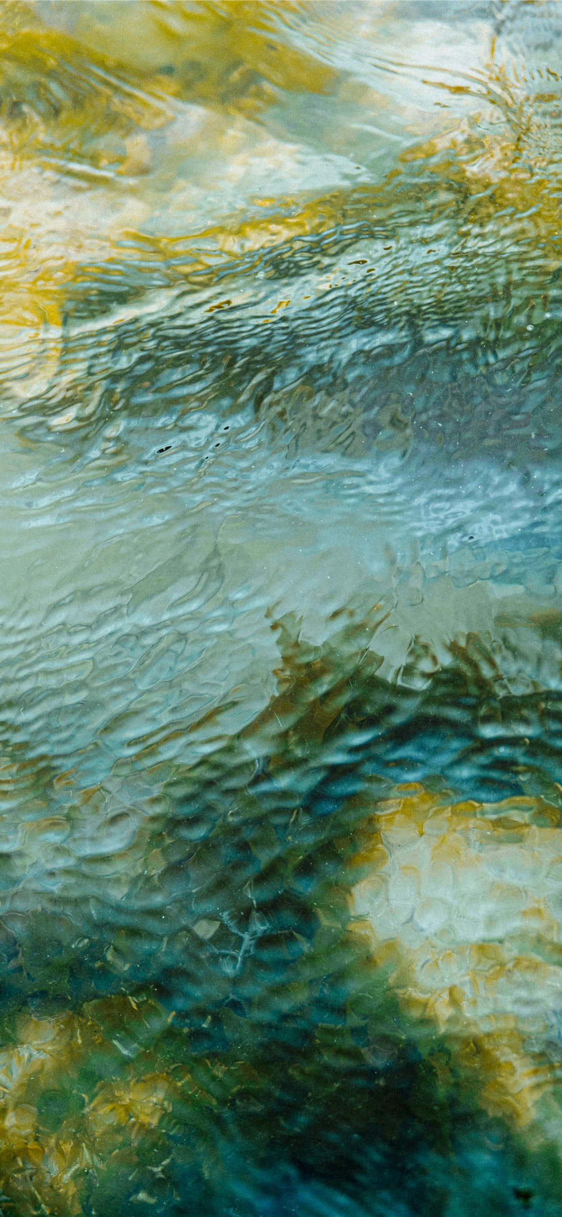 Calming iPhone 桌布 壁紙 — 漣漪扭曲了水面上充滿活力的藍綠色和金色倒影，營造出夢幻般的抽象紋理。