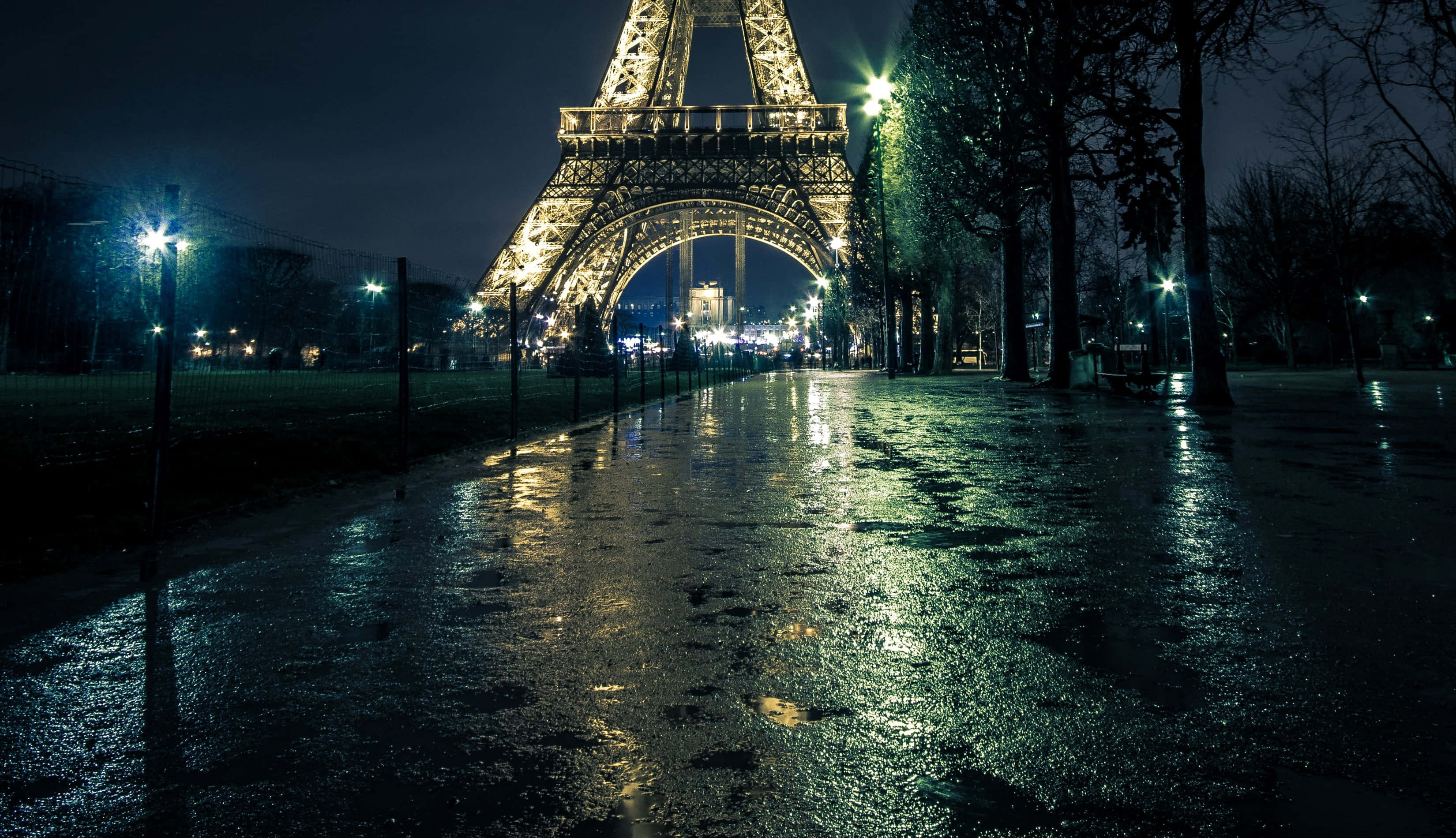 Eiffel Tower 桌布 壁紙 — 潮濕的巴黎小徑在街燈下閃閃發光，通往夜間燈火通明的艾菲爾鐵塔。