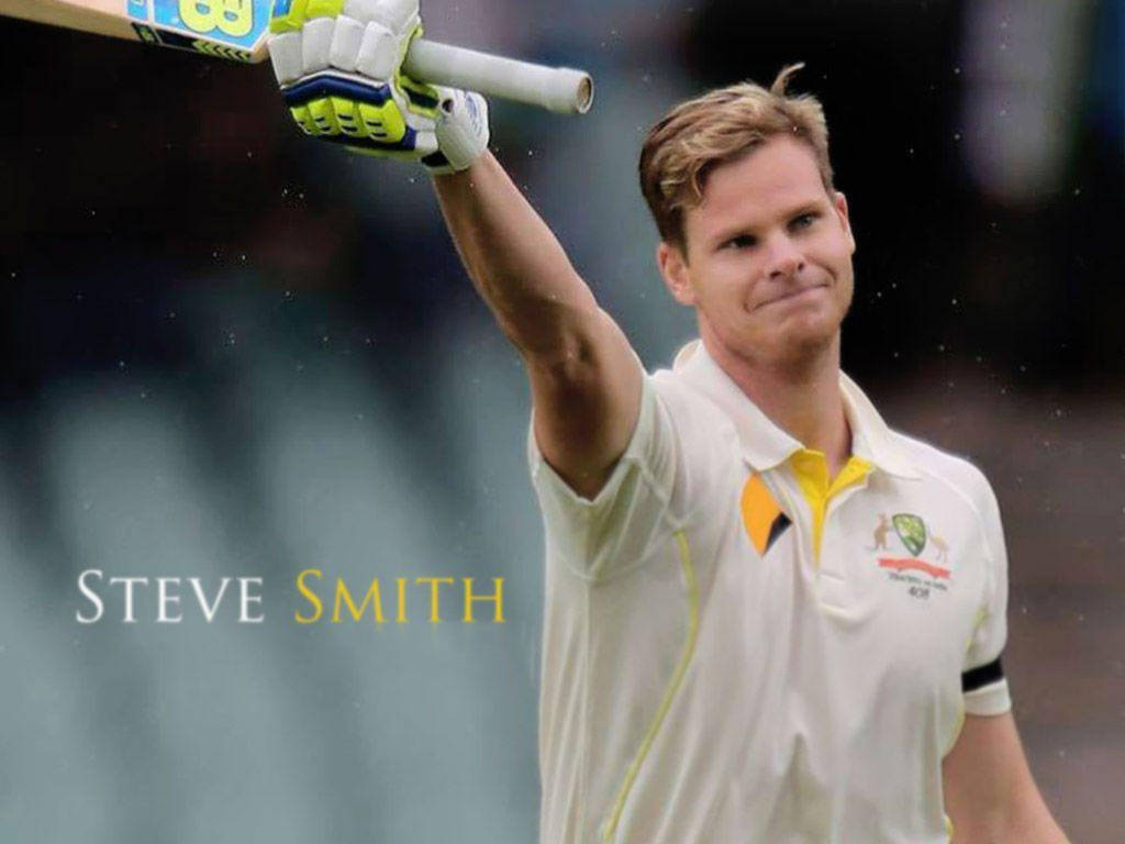 Steve Smith 桌布 壁紙 — 澳洲板球運動員史蒂夫·史密斯身穿白色和黃色制服，在模糊的體育場背景下勝利地舉起球棒。