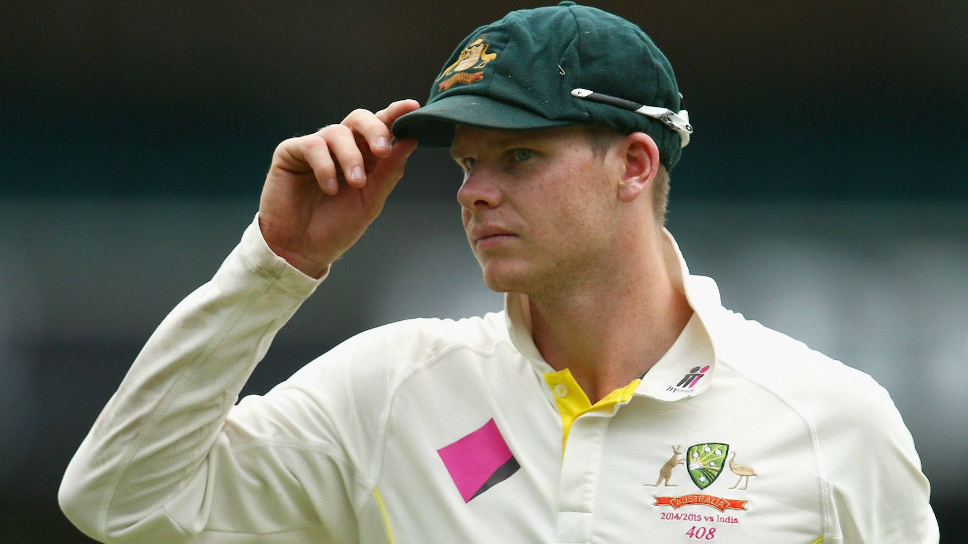 Steve Smith 桌布 壁紙 — 澳洲板球運動員身穿白色制服，專注地傾斜綠色帽子，比賽中神情專注。