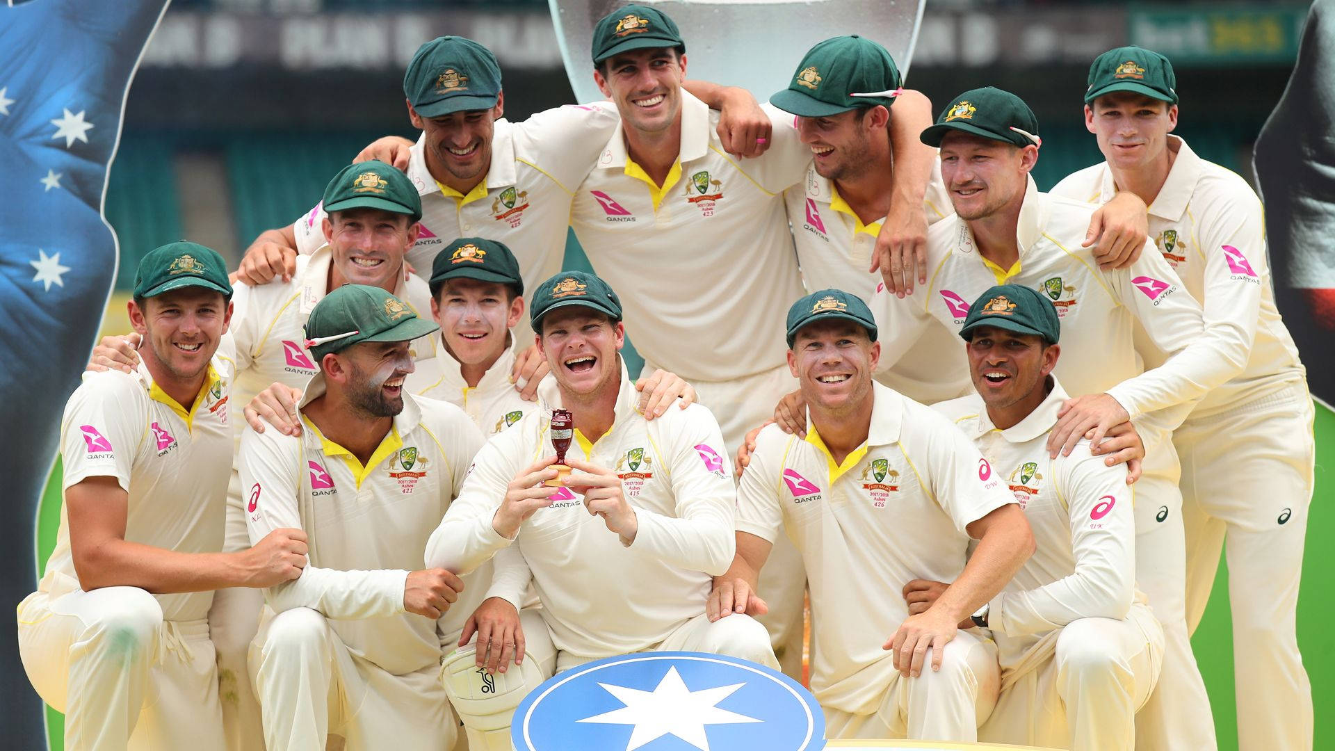 australia cricket 桌布 壁紙 — 澳洲板球隊身穿白色制服、戴綠色帽子，在戶外高舉獎盃慶祝勝利。