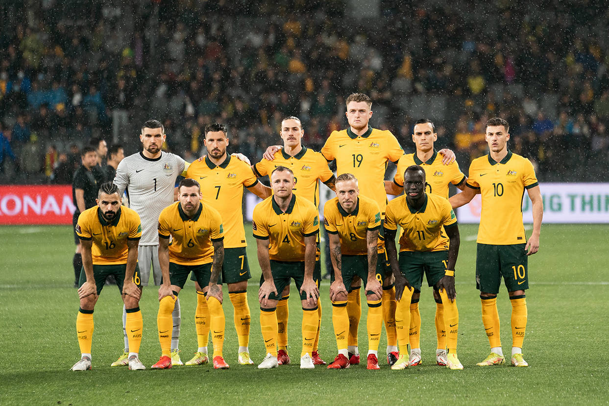 Football Players 桌布 壁紙 — 澳洲足球隊身穿黃色球衣，在明亮的泛光燈下，莊嚴地站在被雨水浸濕的球場上。