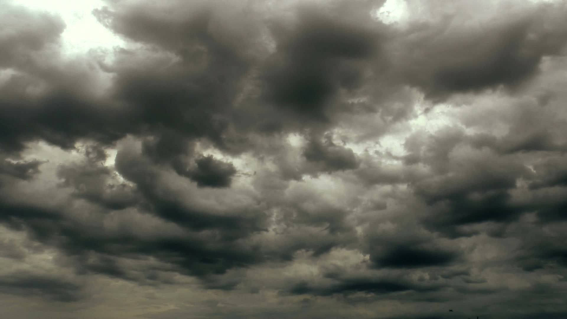 Aesthetic Cloud 桌布 壁紙 — 濃密的黑暗風暴雲在陰沉的灰色天空中戲劇性地旋轉，明亮的陽光斑塊穿透雲層。