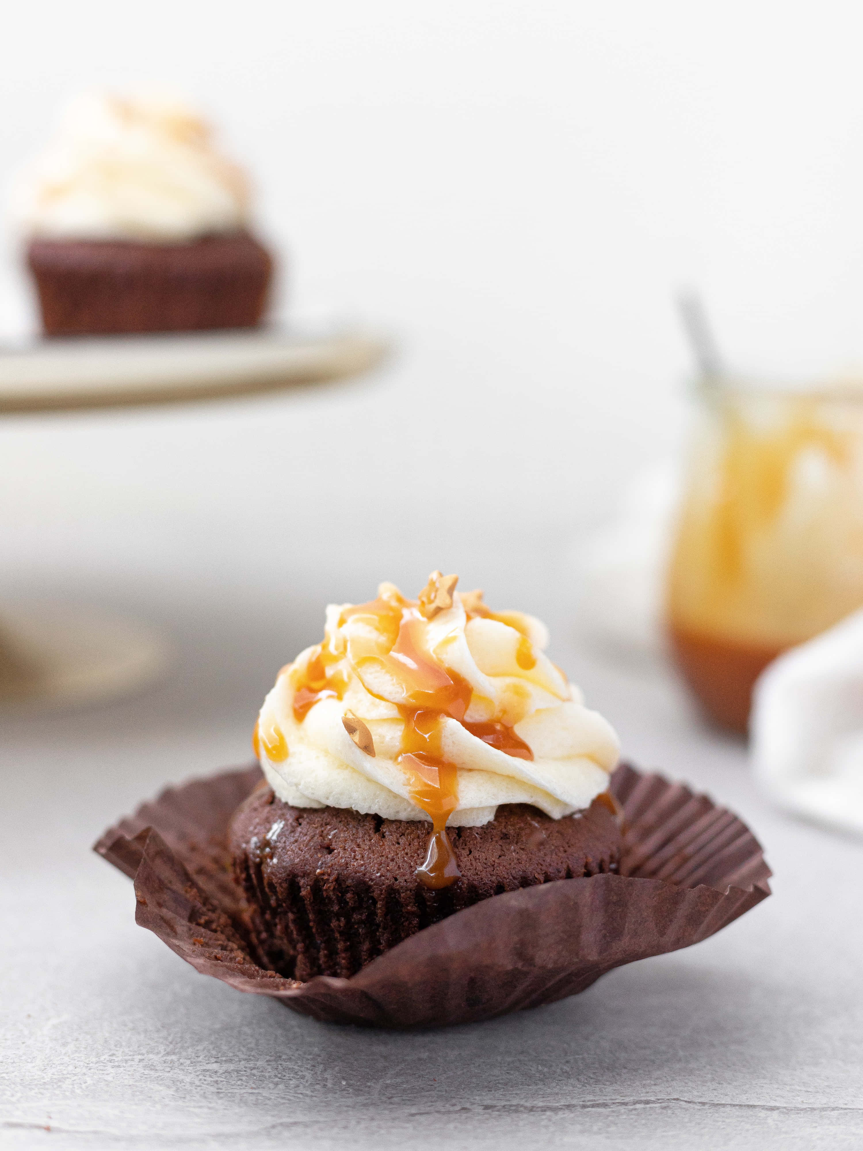Cupcake 桌布 壁紙 — 濃郁巧克力杯子蛋糕，覆蓋著奶油白色糖霜，淋上金黃焦糖，並以烤堅果點綴。