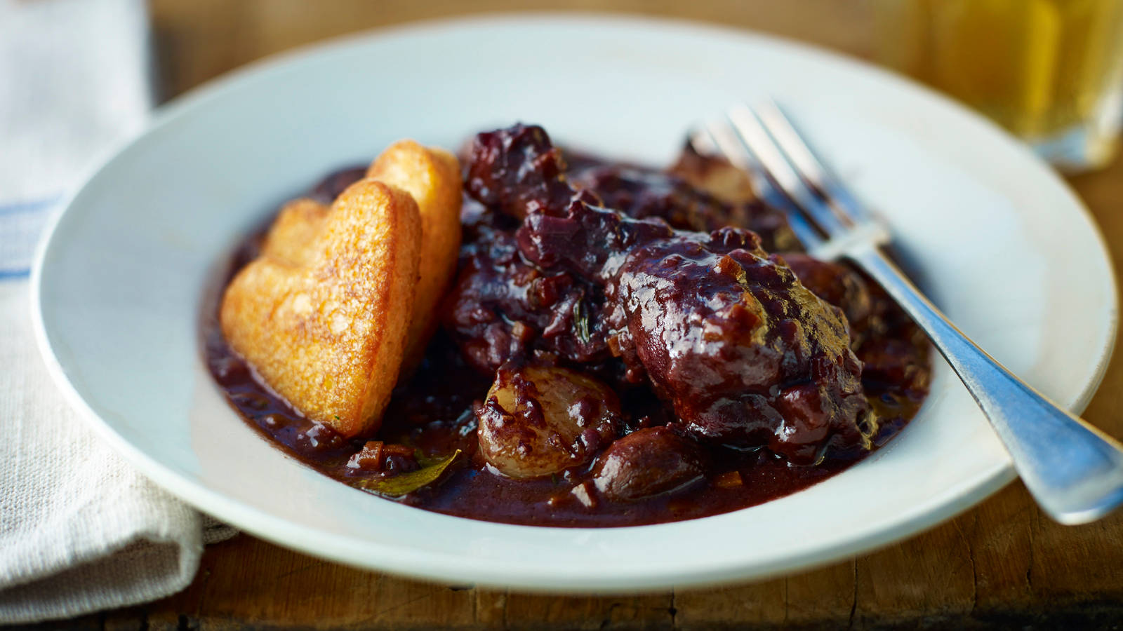Food Photography 桌布 壁紙 — 濃郁深紅色燉牛肉，配上金黃色心形吐司，放在白色盤子上，附有叉子，置於木桌上。