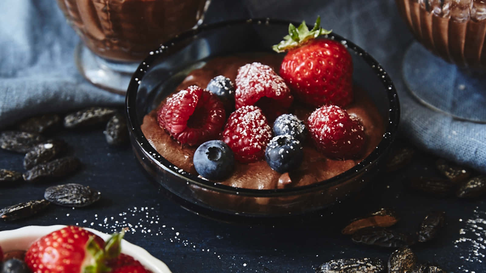 Desserts 桌布 壁紙 — 濃郁的巧克力布丁，上面鋪上新鮮草莓、覆盆子和藍莓，撒上糖粉，置於深色表面上。