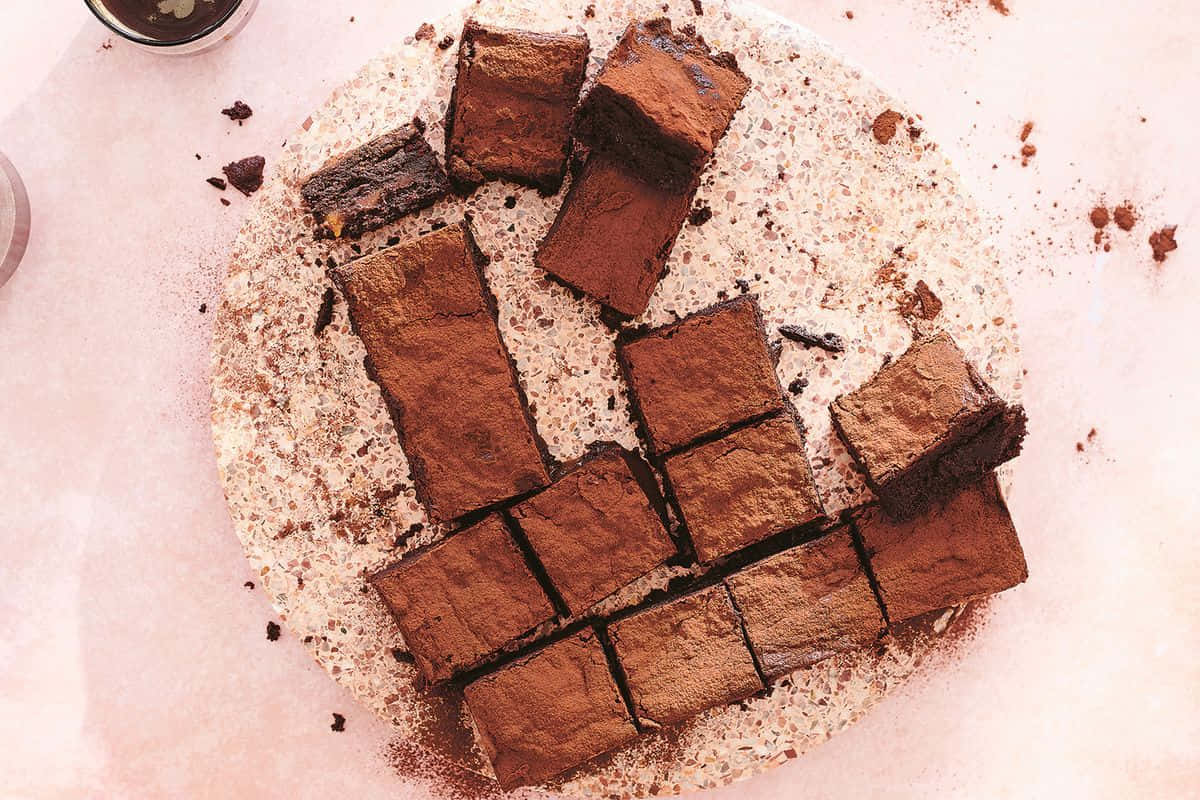 Caramel Brownie 桌布 壁紙 — 濃郁的巧克力布朗尼切成方塊，放在撒有可可粉的斑點盤上。