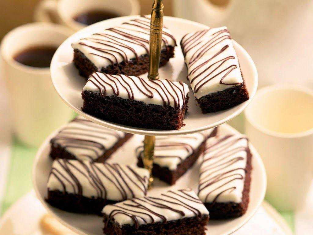 布朗尼 桌布 壁紙 — 濃郁的巧克力布朗尼配上白色糖霜和巧克力淋醬，優雅地擺放在兩層架子上，旁邊有咖啡杯。