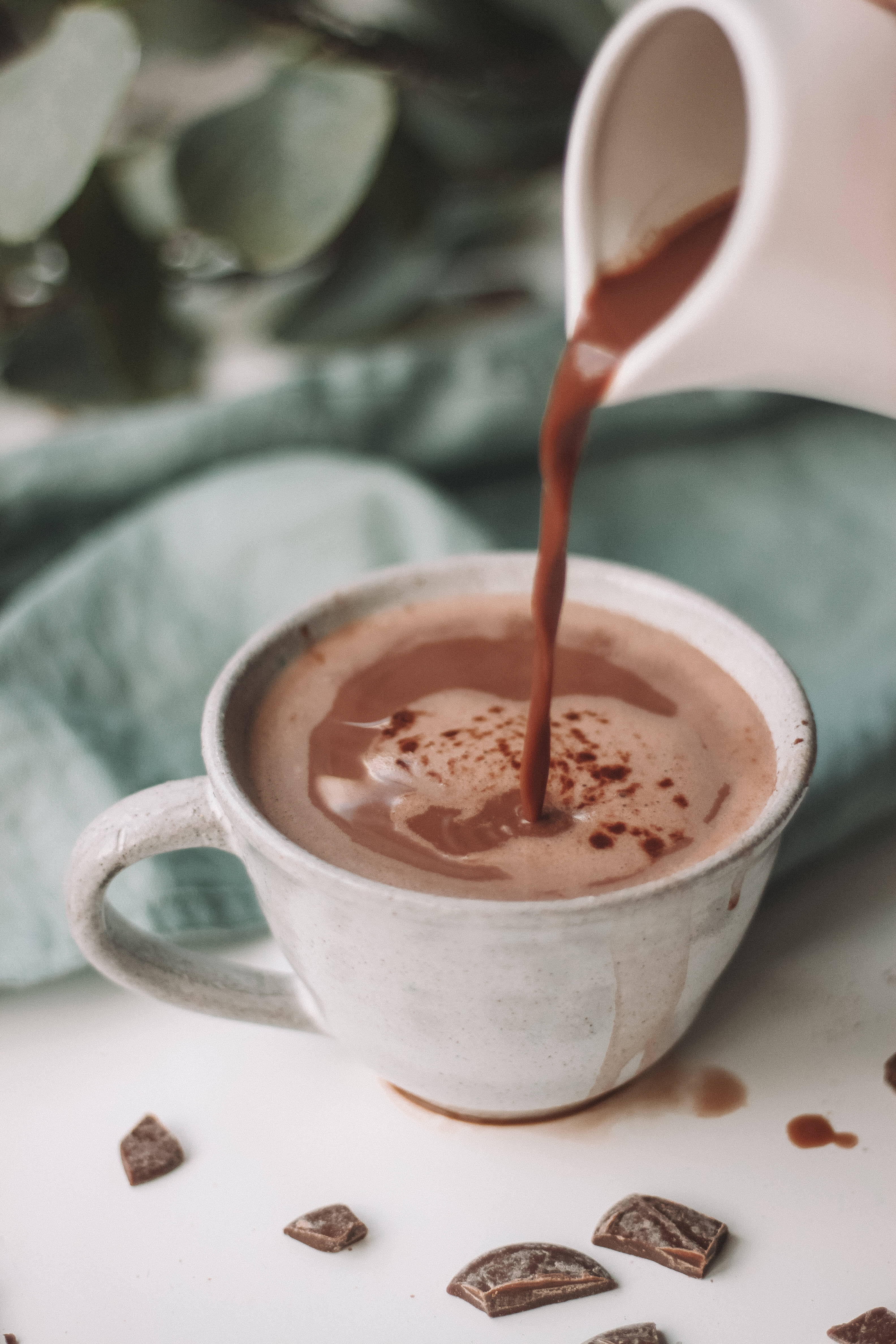 Chocolate 桌布 壁紙 — 濃郁的巧克力從白色壺中倒入鄉村風格的杯子，上面撒有可可粉，周圍散落著巧克力塊。