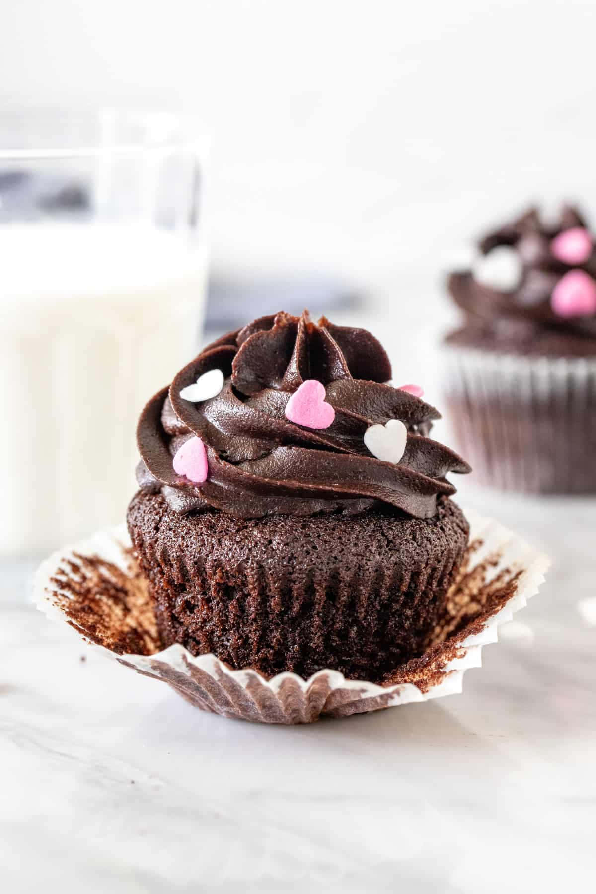 Cupcake 桌布 壁紙 — 濃郁的巧克力杯子蛋糕，上面有深色糖霜漩渦和粉白色心形裝飾，旁邊放著一杯牛奶，置於大理石表面上。