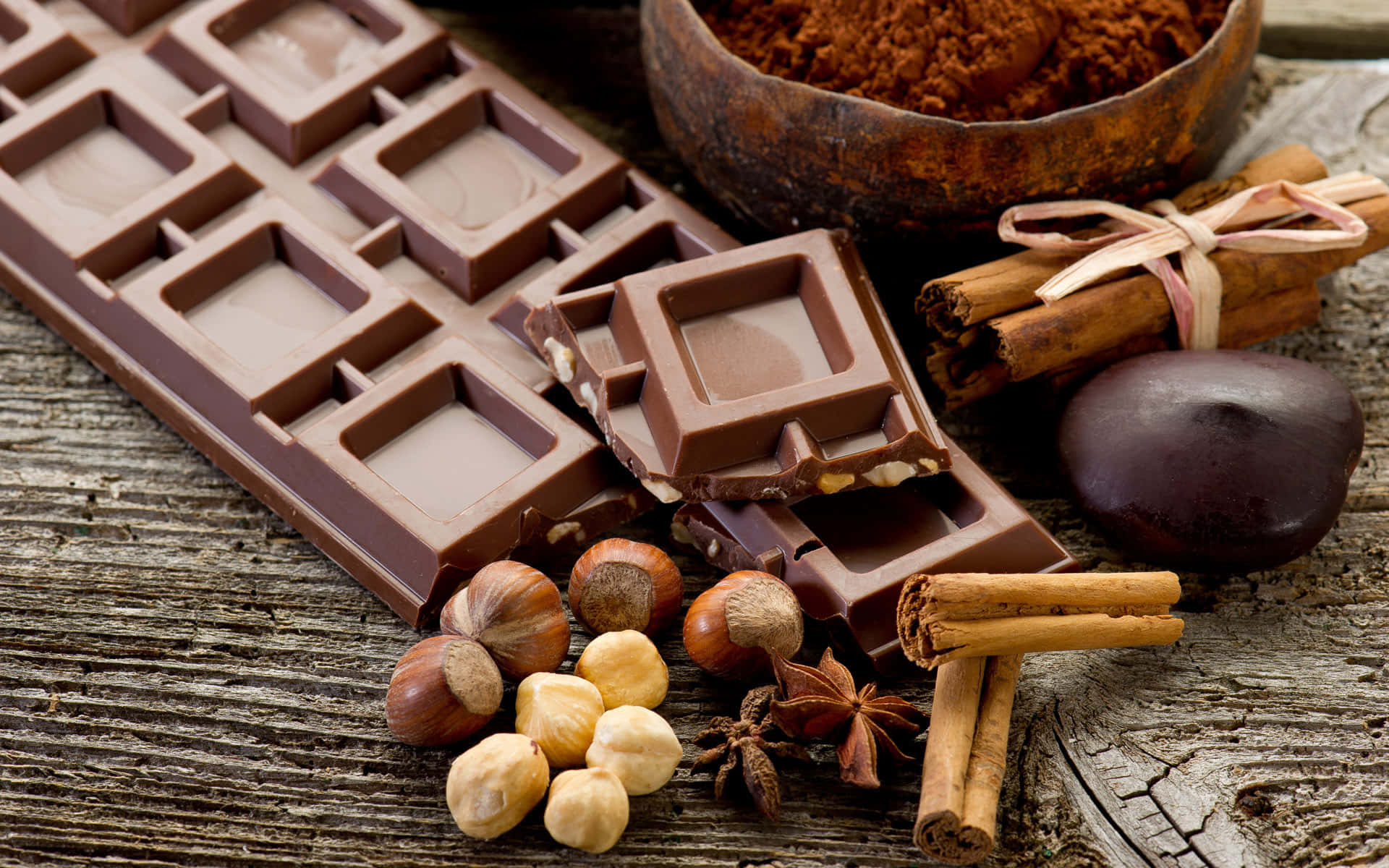 Brown Chocolate 桌布 壁紙 — 濃郁的巧克力條和肉桂、榛子等香料放在經風化的木質表面上。