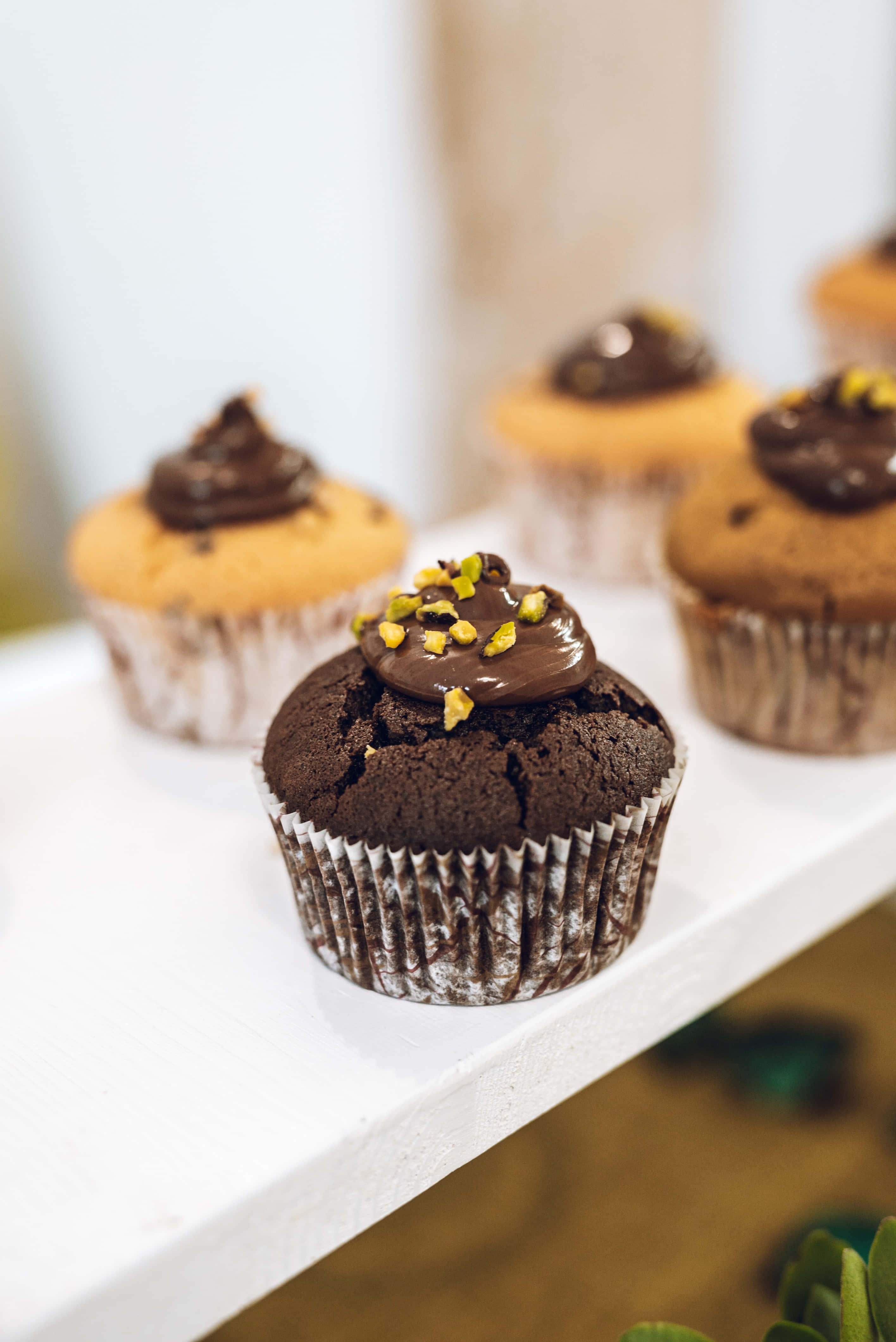 Cupcake 桌布 壁紙 — 濃郁的巧克力紙杯蛋糕，上面鋪滿光澤的糖霜和開心果碎，誘人地放在白色架子上。