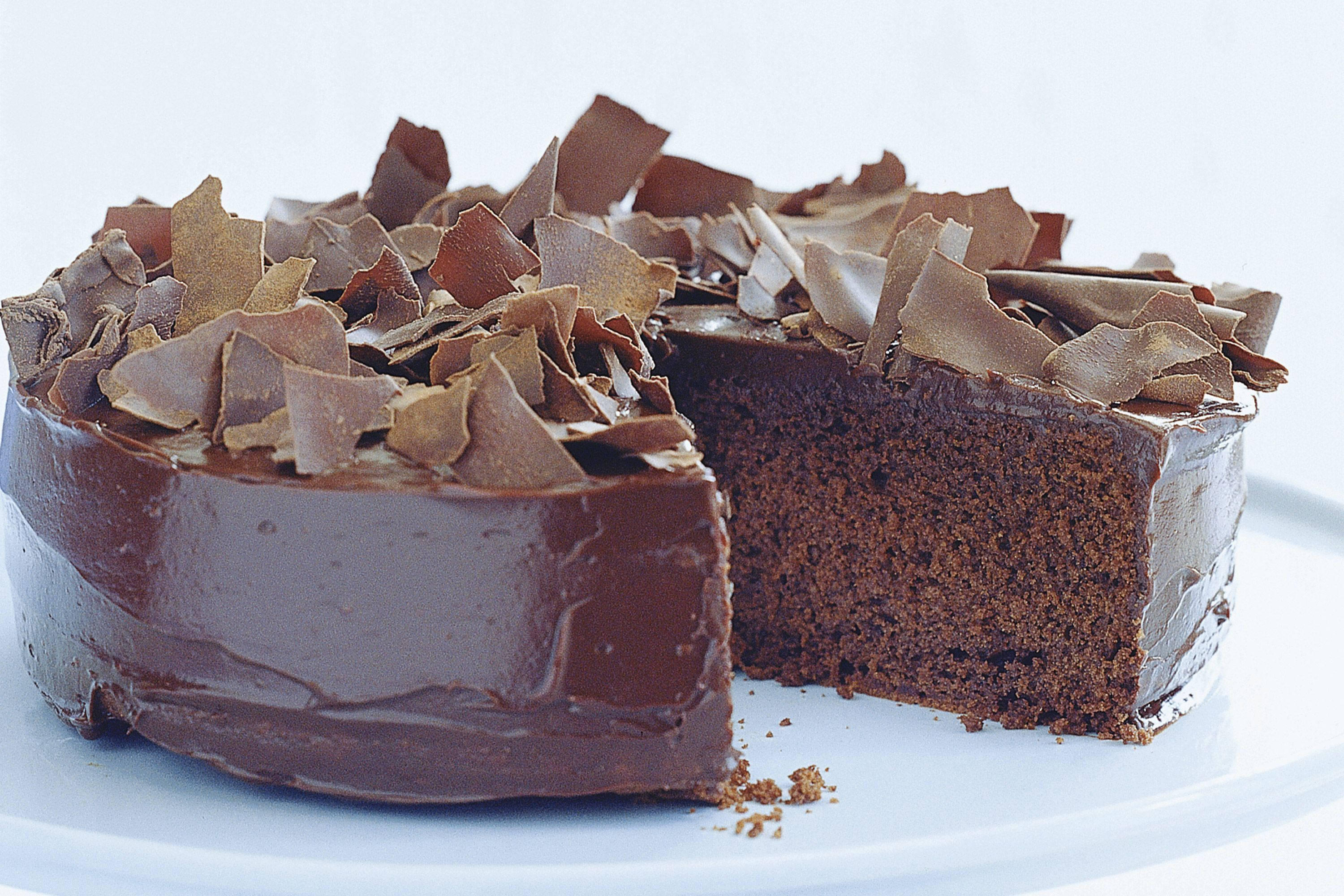 Chocolate Cake 桌布 壁紙 — 濃郁的巧克力蛋糕，帶有光澤的糖霜和散落的巧克力碎屑，放在白色盤子上，其中一塊已被切走。