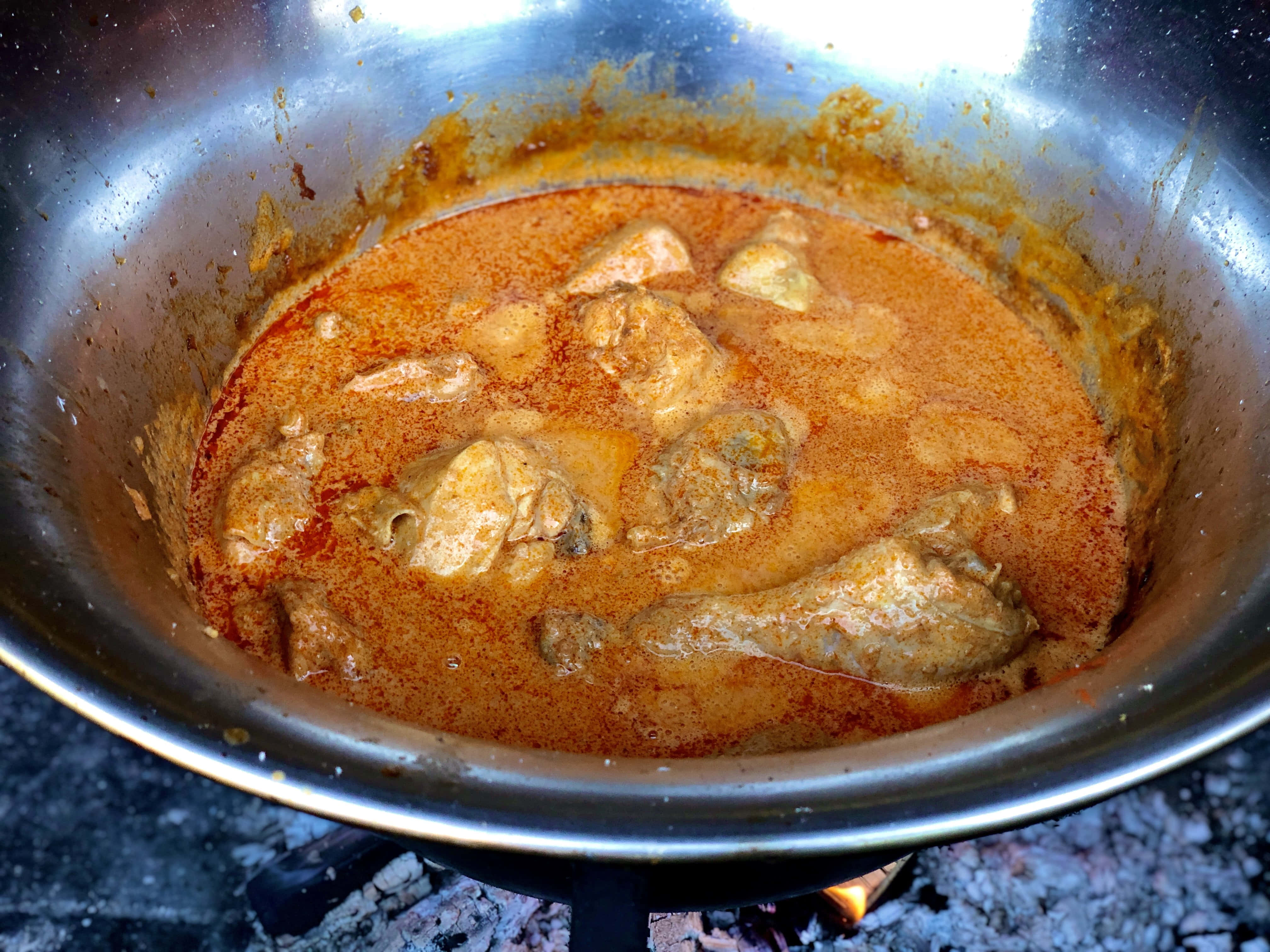 Chicken 桌布 壁紙 — 濃郁的橙色咖哩在營火餘燼上，於不鏽鋼鍋中慢燉。