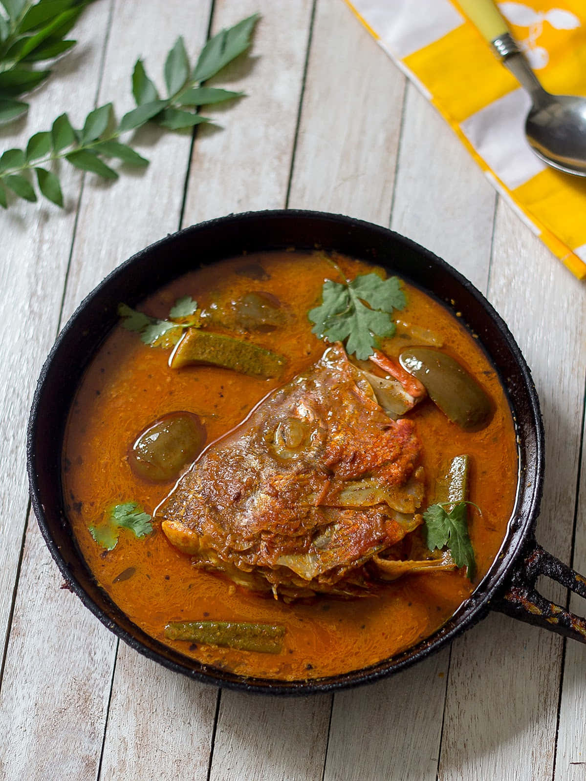 Food Photography 桌布 壁紙 — 濃郁的橙色魚咖哩，搭配青辣椒和香菜，盛裝在黑色煎鍋中，置於風化的木桌上。