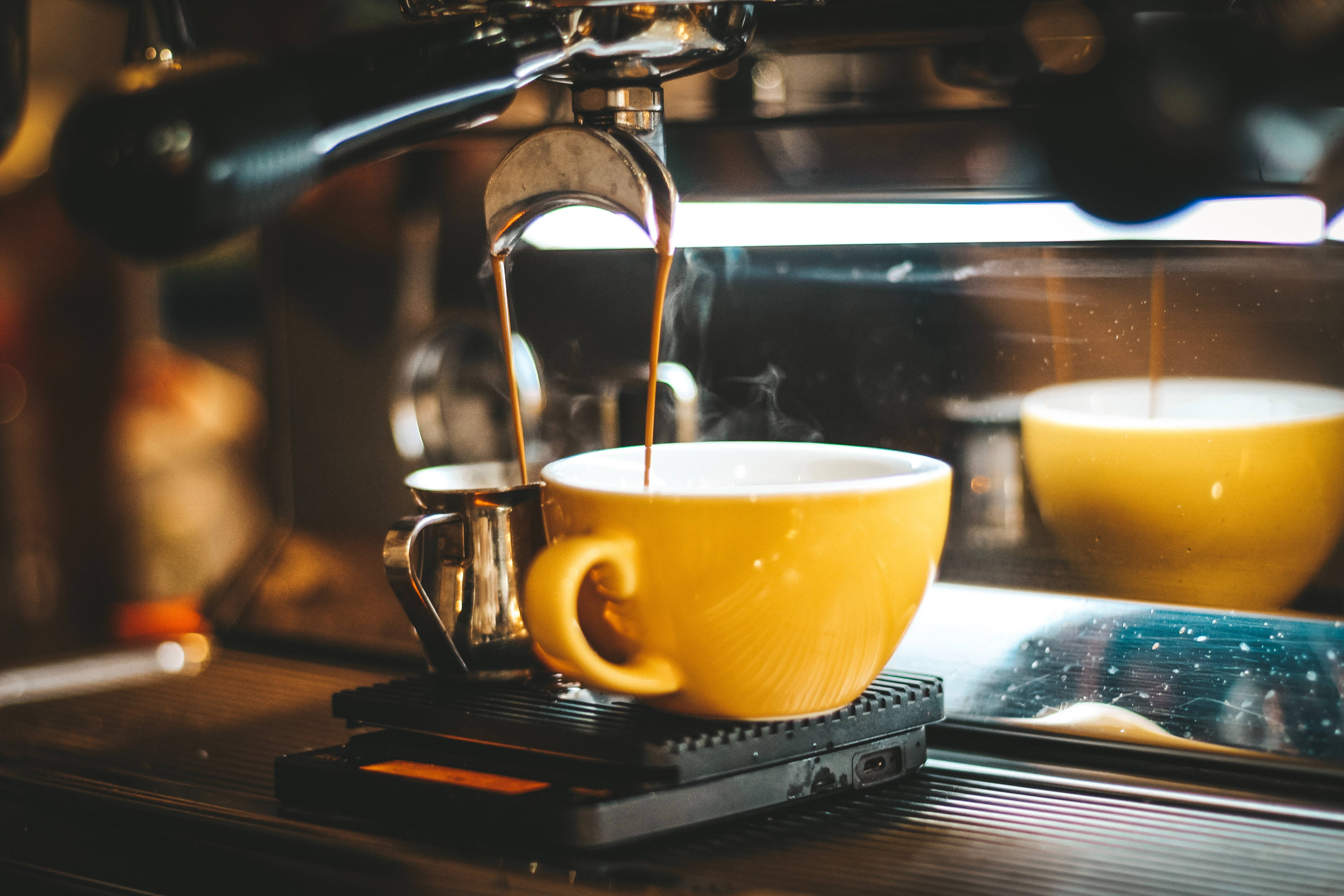 Coffee Shop 桌布 壁紙 — 濃郁的濃縮咖啡流入咖啡機上一個充滿活力的黃色杯子，蒸氣在溫暖的金色光線中升起。