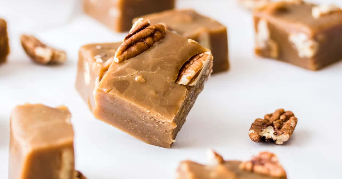 Penuche Fudge 桌布 壁紙 — 濃郁的焦糖軟糖方塊，上面放有山核桃，置於明亮的白色表面上，周圍散落著堅果。