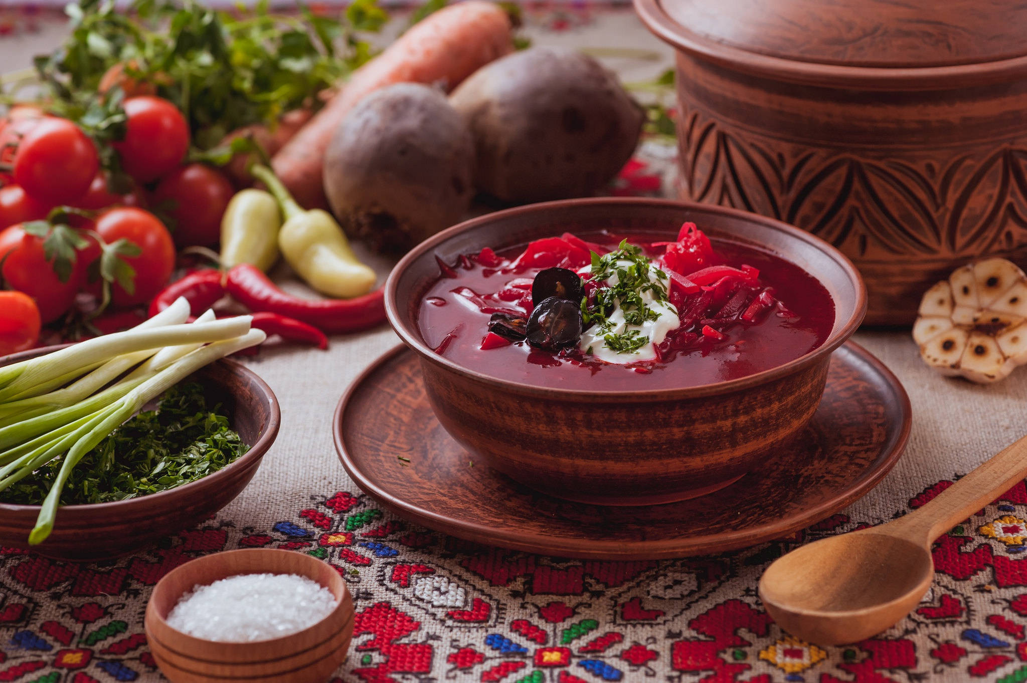 beetroot 桌布 壁紙 — 濃郁的紅菜湯盛在木碗中，飾以酸奶油和香草，周圍是新鮮蔬菜，放在色彩繽紛的刺繡桌布上。