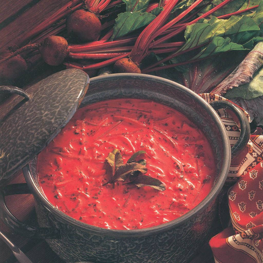beetroot 桌布 壁紙 — 濃郁的紅菜頭湯盛在深色陶瓷鍋中，以香草裝飾，周圍是新鮮的紅菜頭和蔬菜。