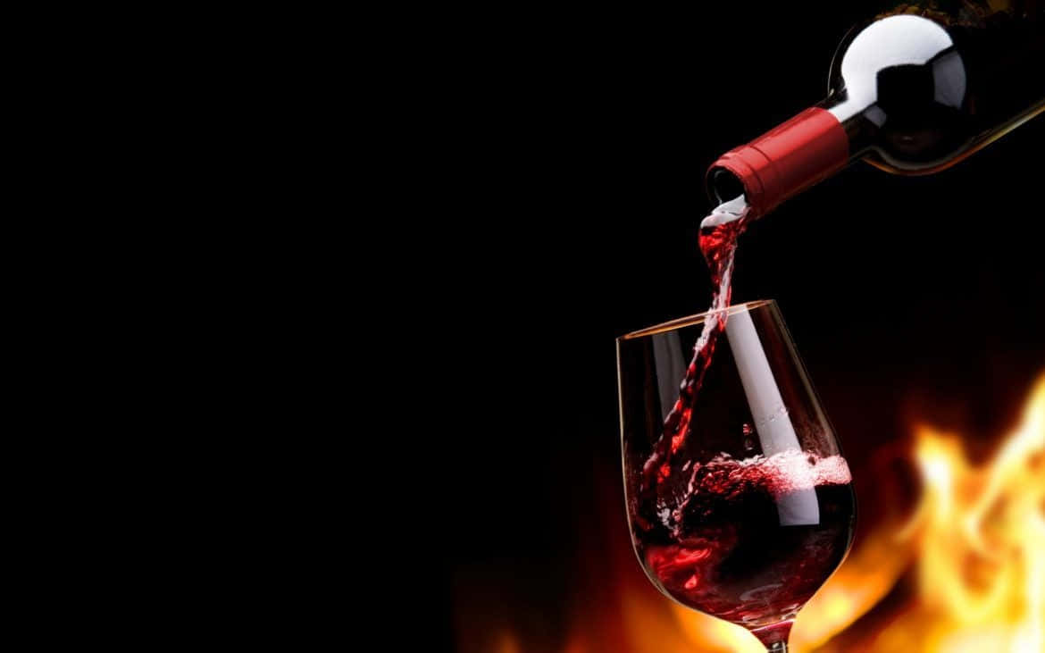 Red Wine Glass 桌布 壁紙 — 濃郁的紅酒從酒瓶倒入玻璃杯中，背景昏暗，溫暖的爐火在後方閃耀。