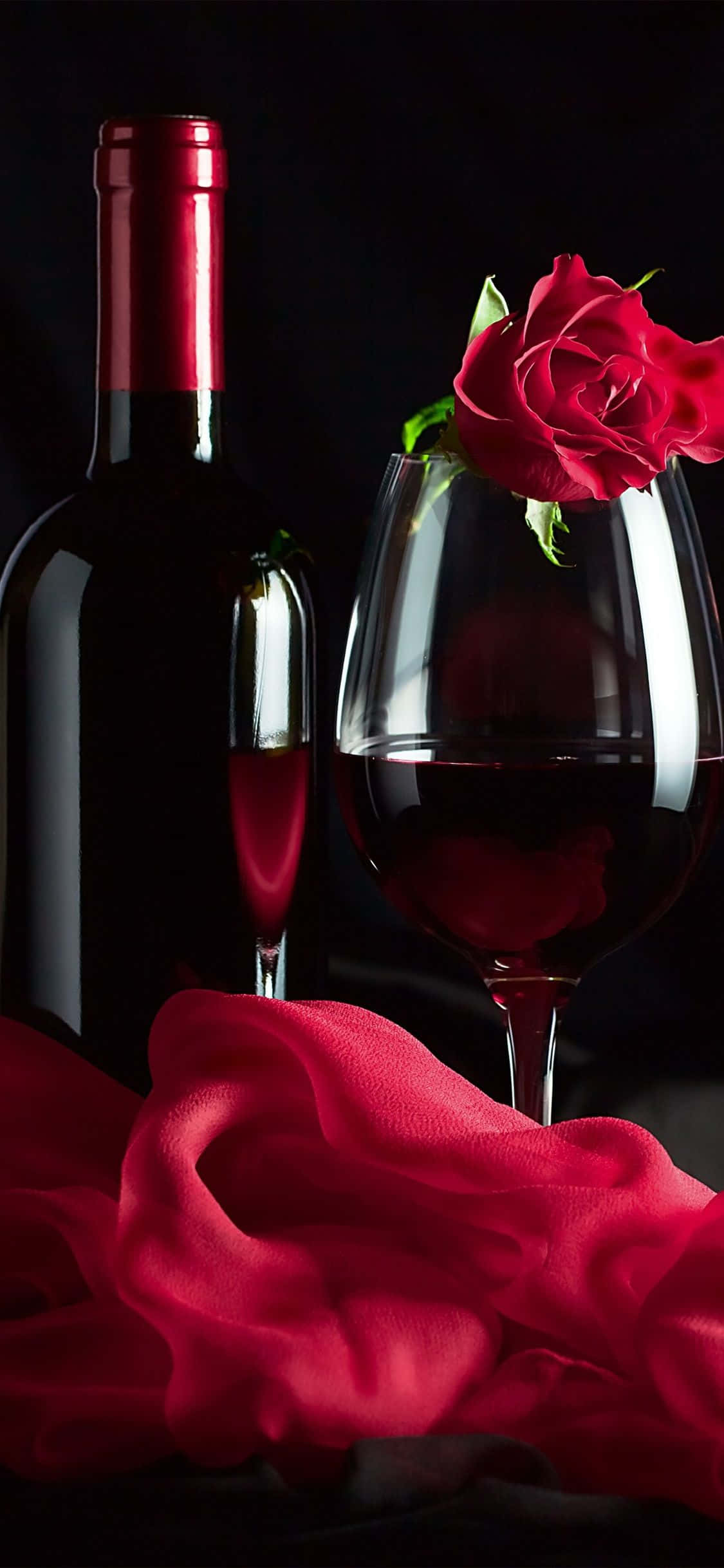 Red Wine Glass 桌布 壁紙 — 濃郁的紅酒瓶和酒杯，搭配玫瑰與絲綢布料，在深色背景下呈現。