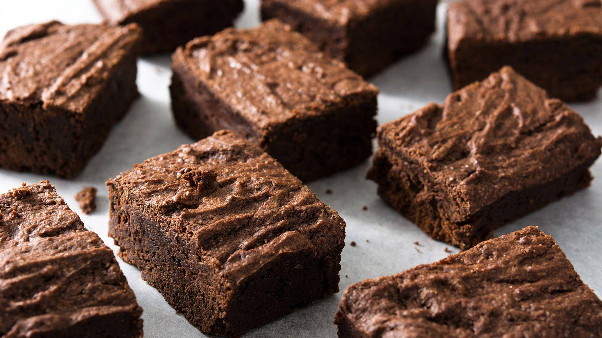 Brownies 桌布 壁紙 — 濃郁的軟心布朗尼，帶有裂紋的巧克力頂部，放在烘焙紙上，特寫鏡頭。