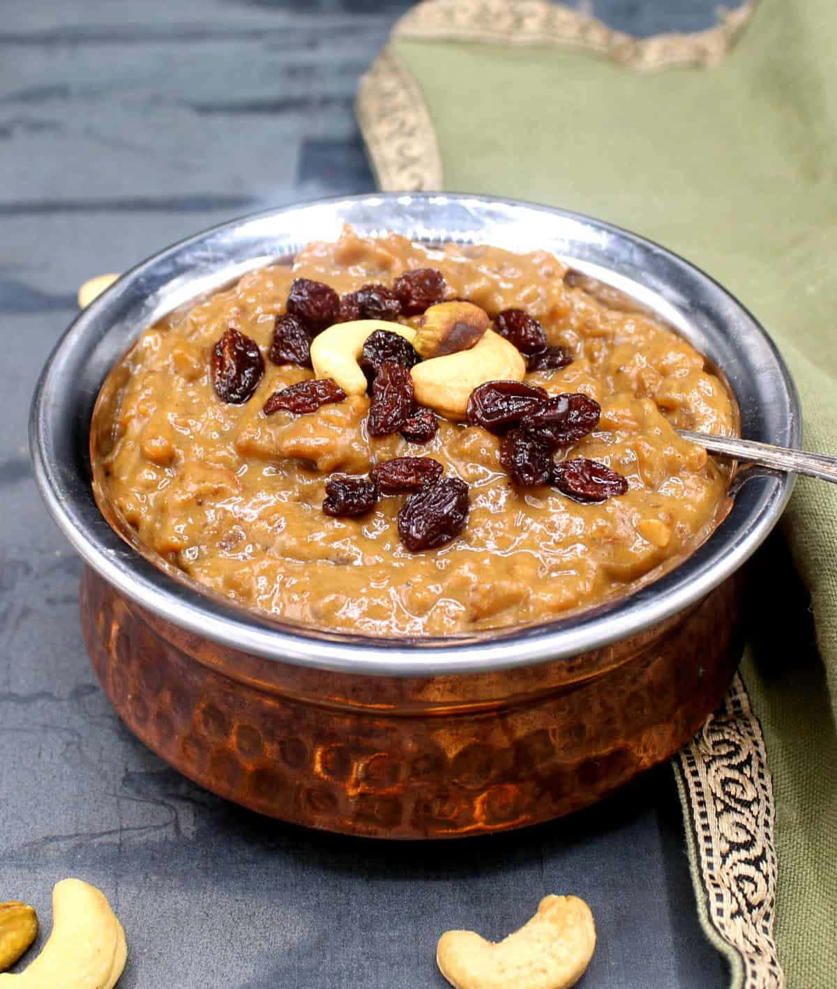 Pongal 桌布 壁紙 — 濃郁的金黃色kheer，上面放有葡萄乾和腰果，盛載於錘紋銅碗中，置於深色石板表面上。